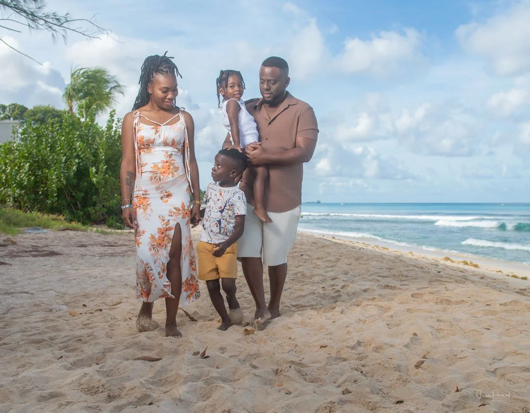 A family of five walking on the beach, with the ocean and partly cloudy sky in the background.