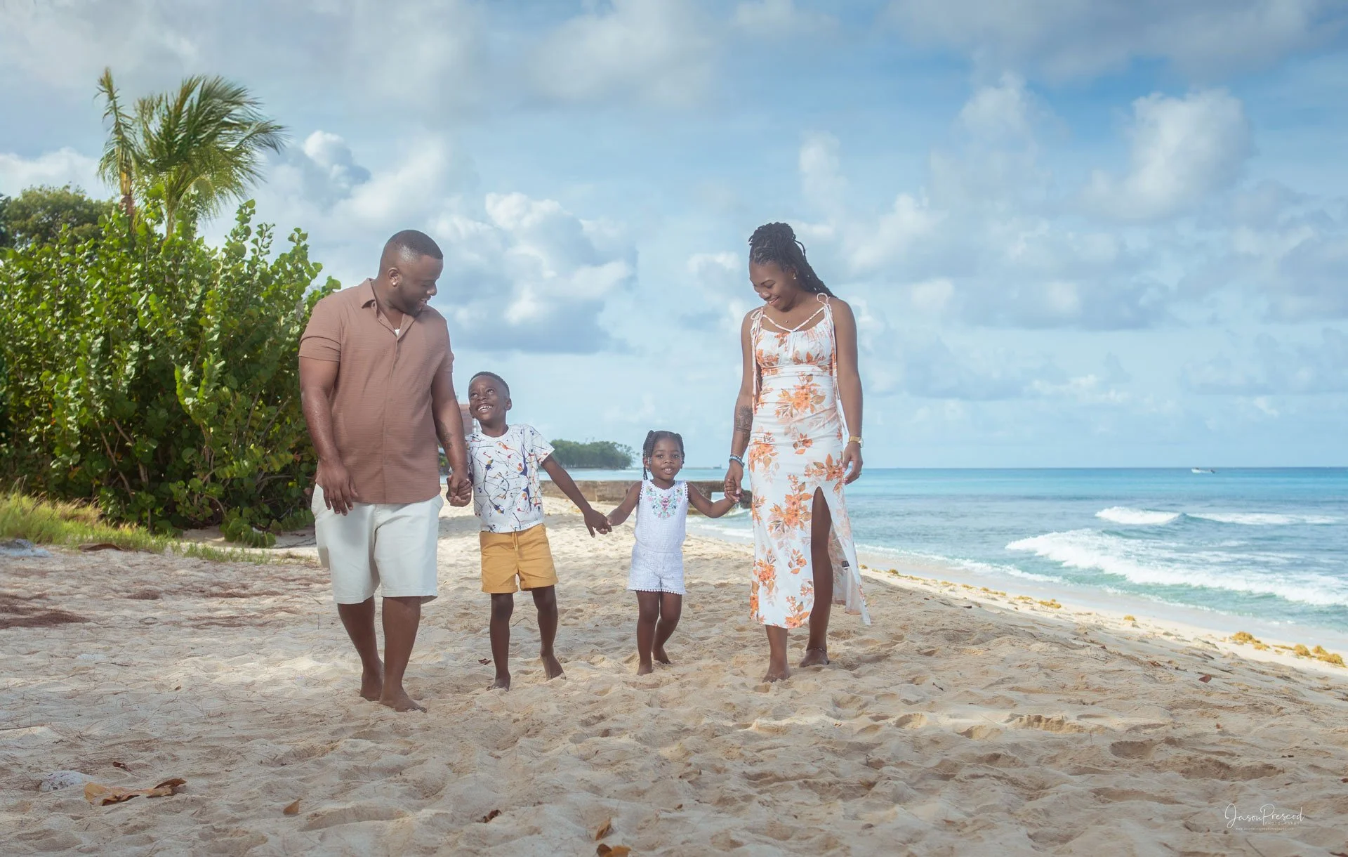 A family of five, including two children, walking hand-in-hand along a sandy beach with ocean waves and blue sky in the background.