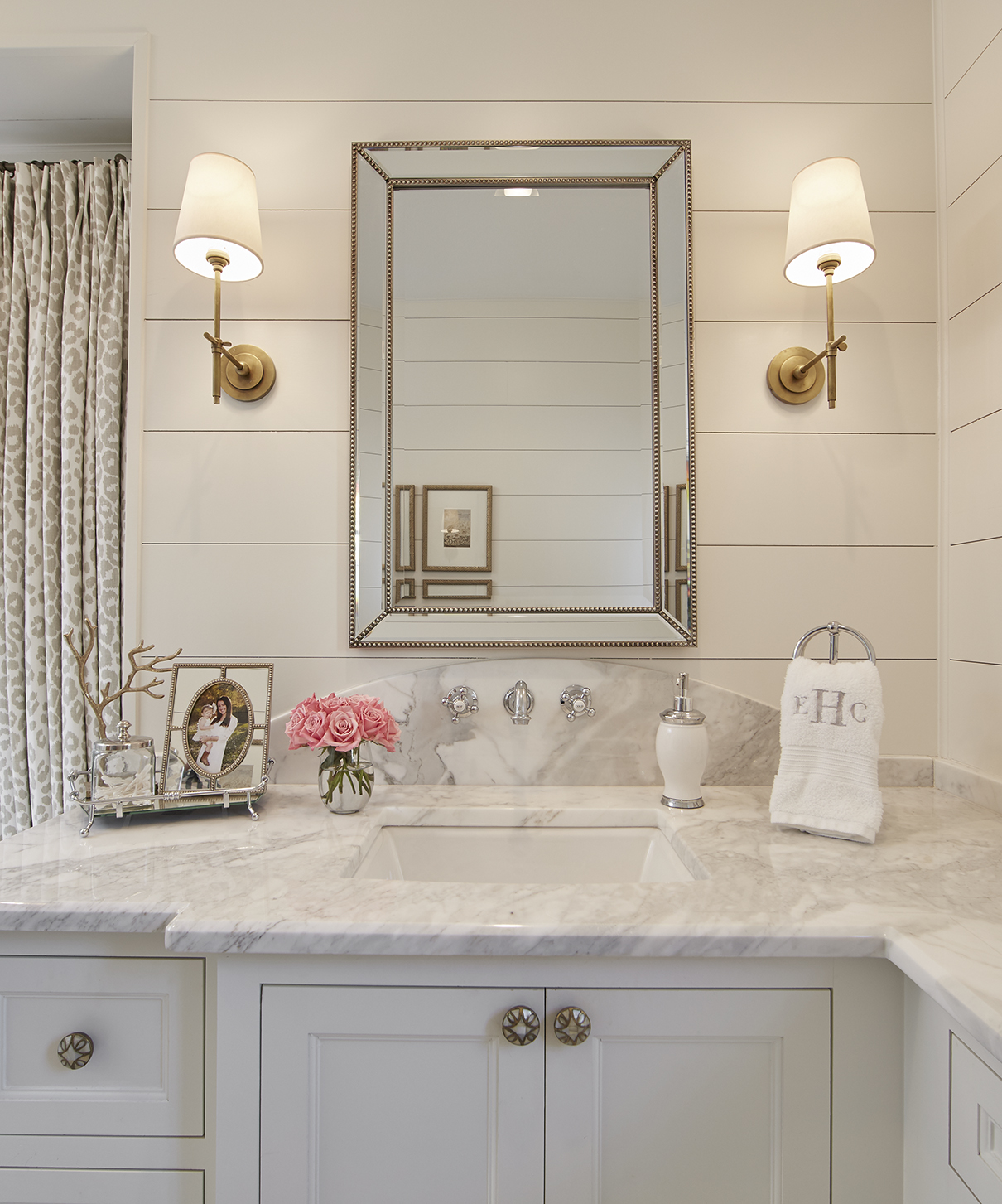 The master bathroom has a glamorous feel with its marble countertops, gold accents and original porcelain hexagon floor tiles. The white shiplap walls tie the room in with the styling of the rest of the house.