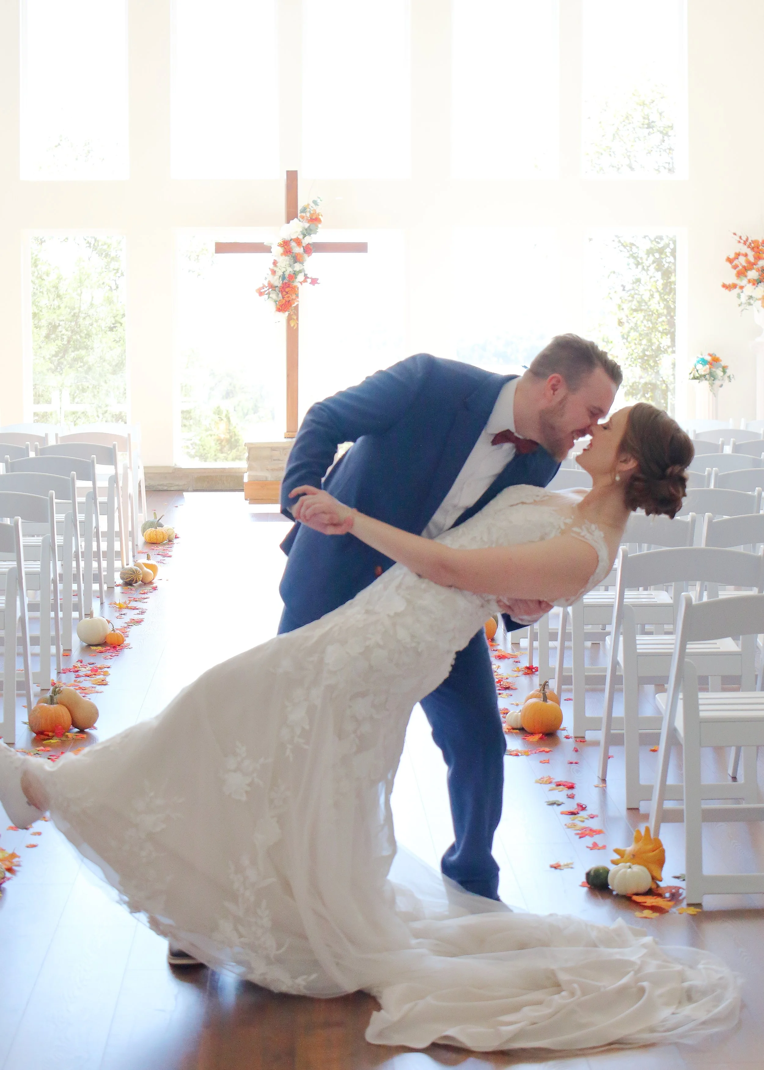 A newlywed couple dancing inside a church with decorated pumpkins and fall leaves on the aisle.