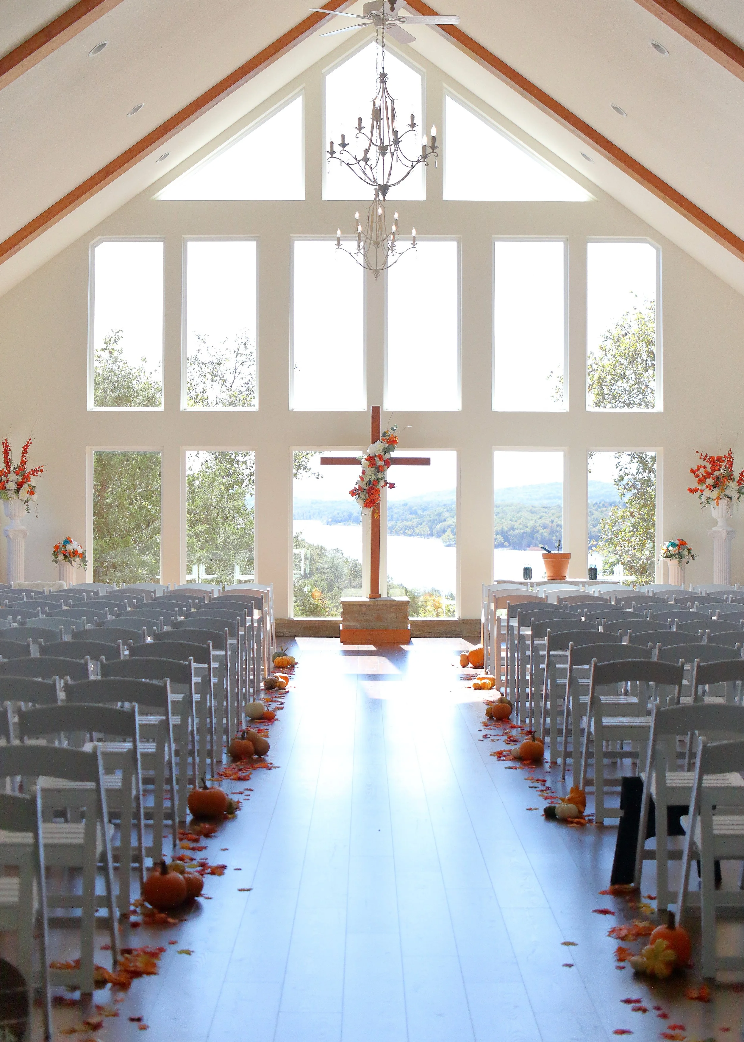 Inside a church with a tall ceiling and large windows. Decorated for fall with pumpkins and leaves along the aisle.