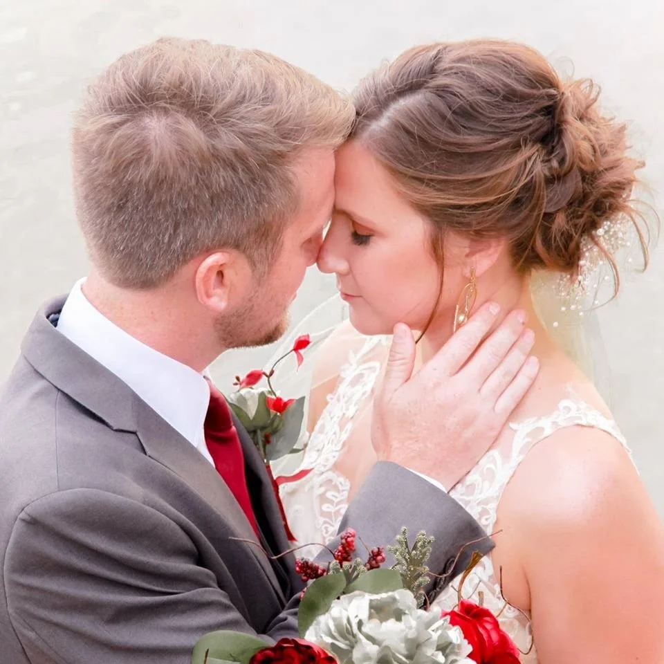 A bride and groom share a close, intimate moment with their foreheads touching and eyes closed on a beach.