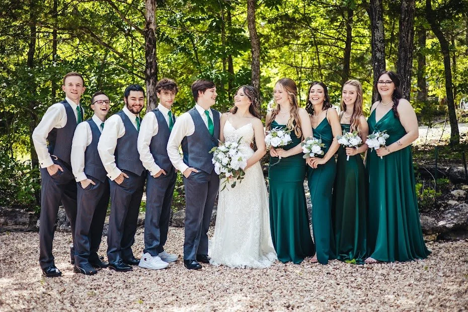 Group of people dressed in formal attire for a wedding in a wooded outdoor setting.