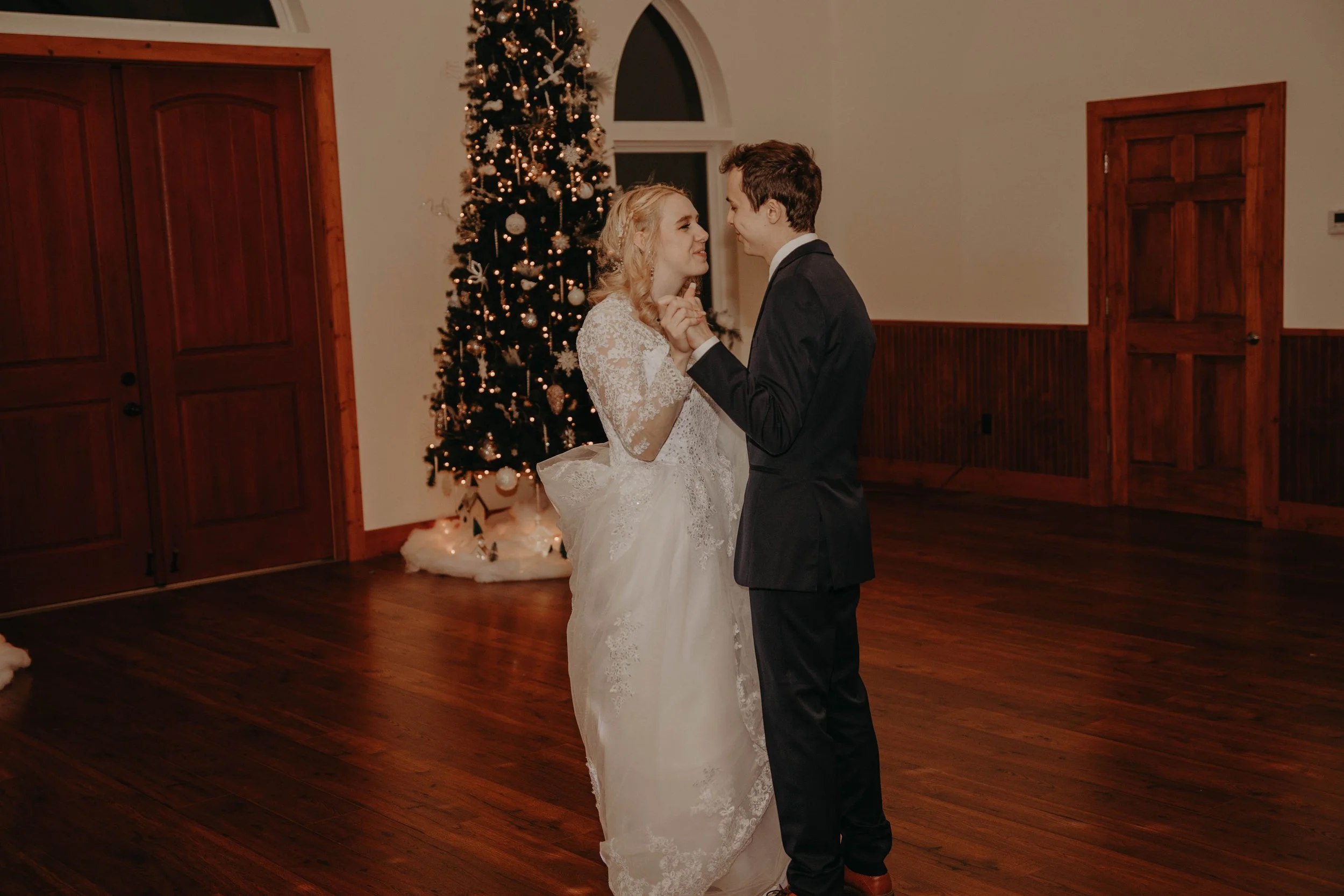 A bride and groom dancing together indoors in front of a decorated Christmas tree.