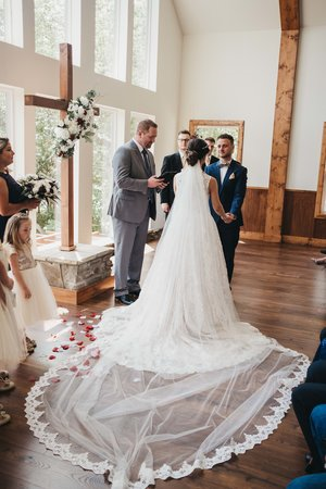 A wedding ceremony inside a bright, wood-paneled church with a bride and groom exchanging vows, surrounded by wedding officiants, bridesmaids, and groomsmen.