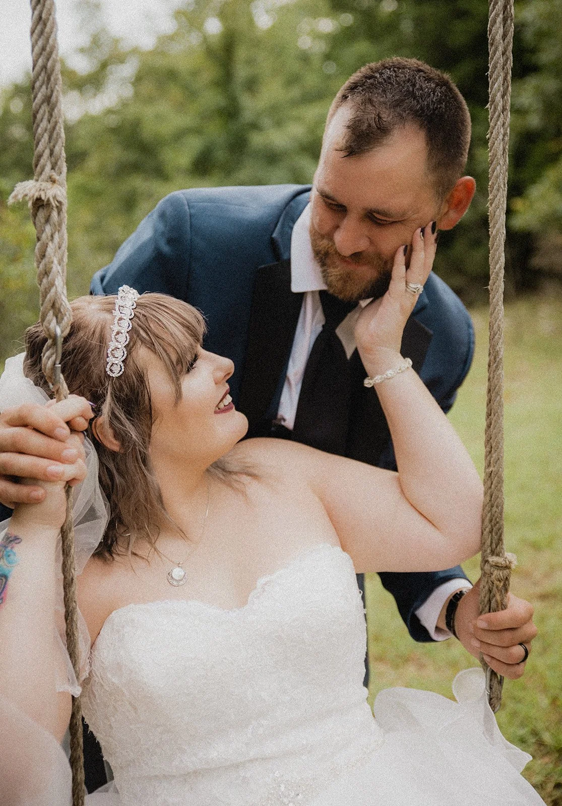A bride and groom sharing a romantic moment outdoors on a swing, with the bride smiling up at the groom who is gazing down at her.