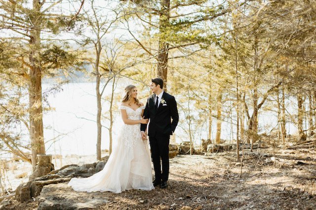 A bride and groom holding hands and sharing a moment in a wooded outdoor setting.