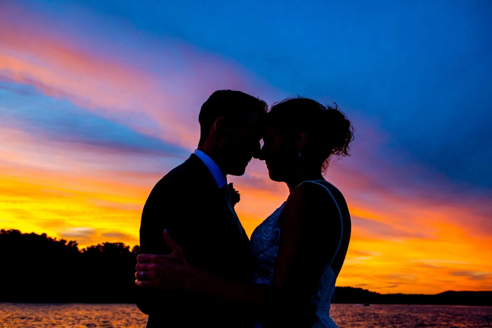 Silhouette of a couple embracing against a colorful sunset sky.