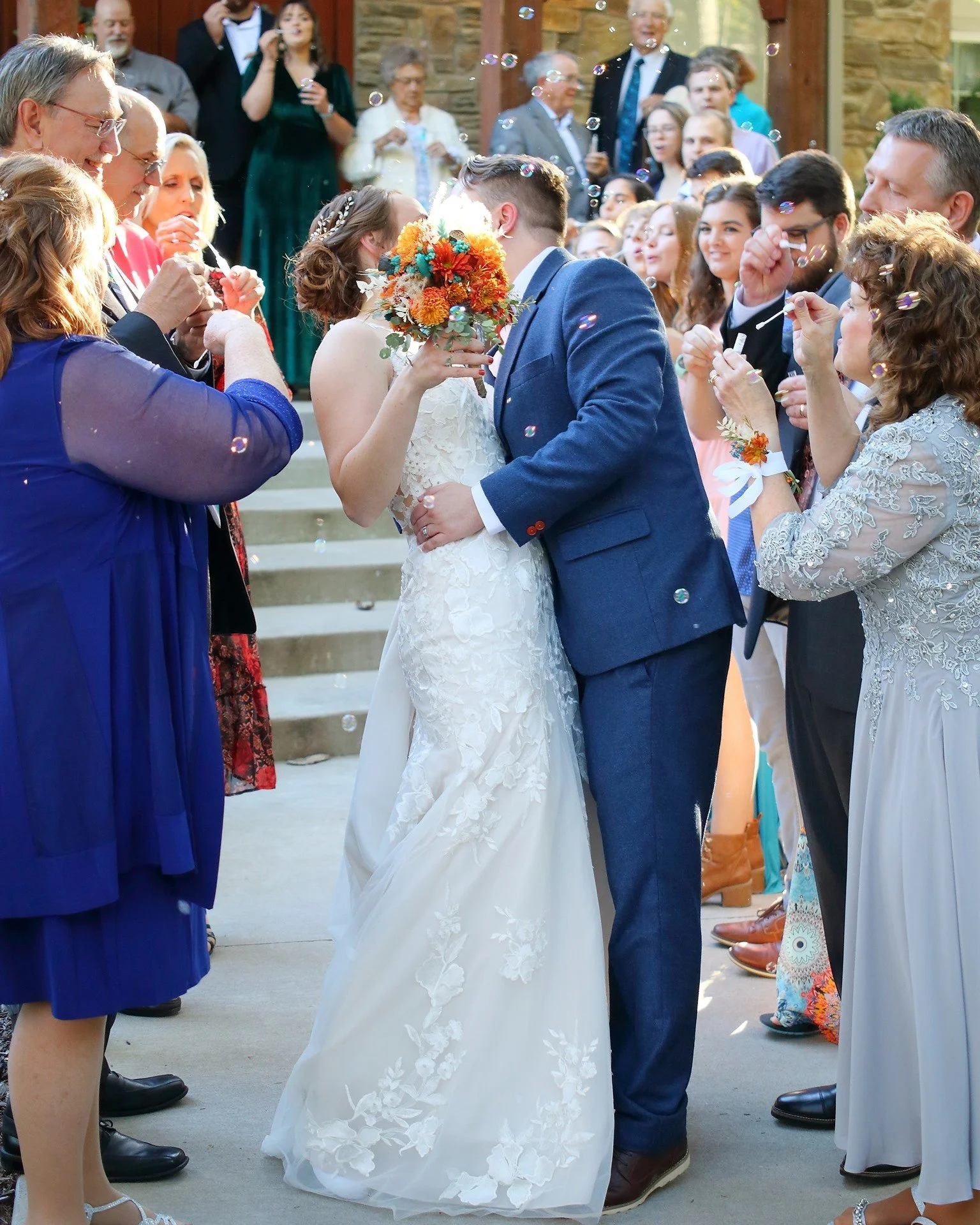 Bride and groom kissing at their wedding reception surrounded by friends and family.