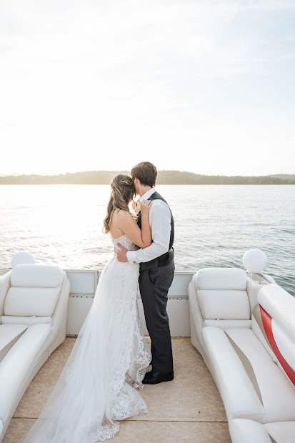 Bride and groom kissing on a boat with water and distant shoreline in the background.