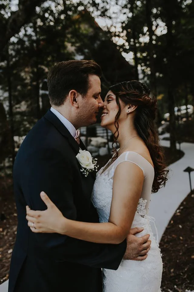 A bride and groom in wedding attire embracing outdoors at sunset