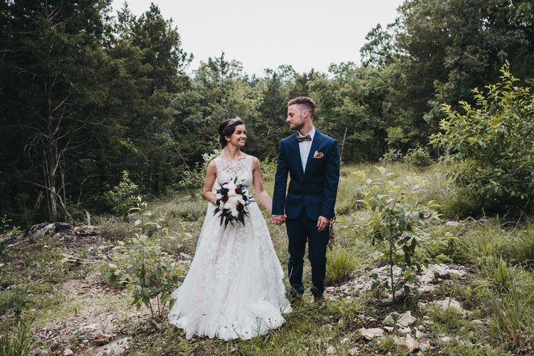 Bride and groom holding hands and walking in a forested area on their wedding day.