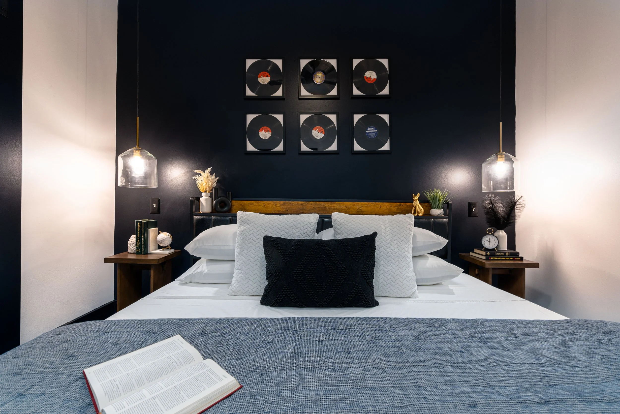 Saint Philip suite with layered white bedding, a charcoal accent wall, pendant lights, and framed record artwork.