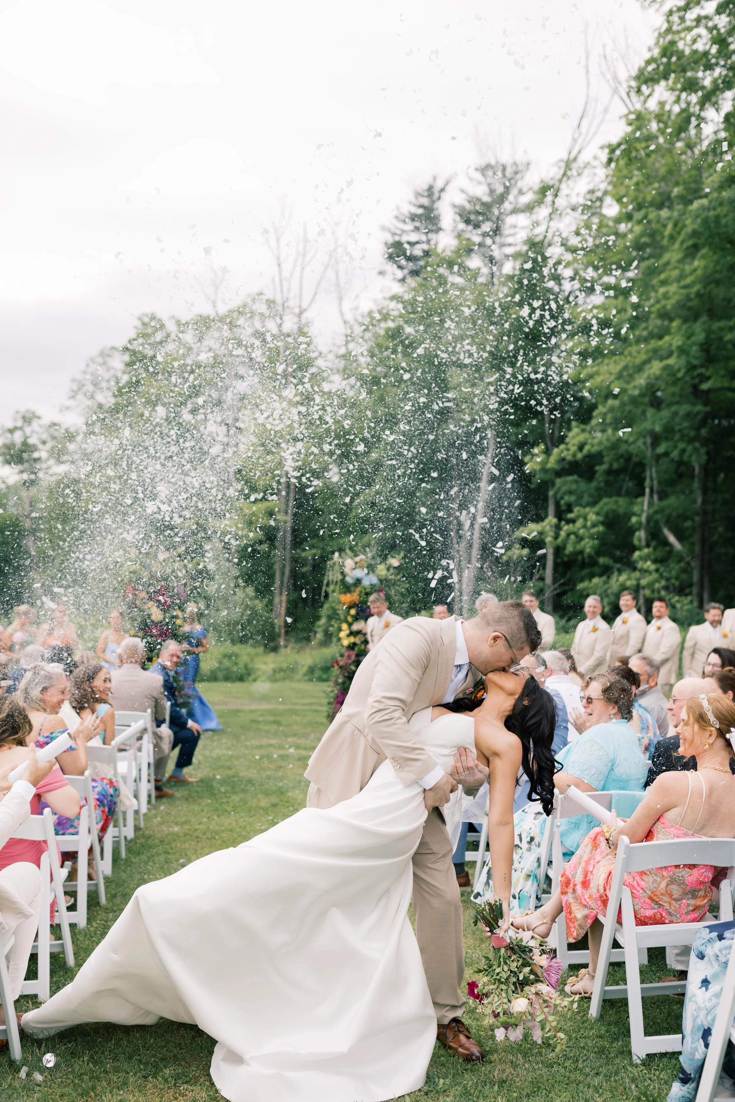 bride and groom kissing at wedding aisle with confetti
