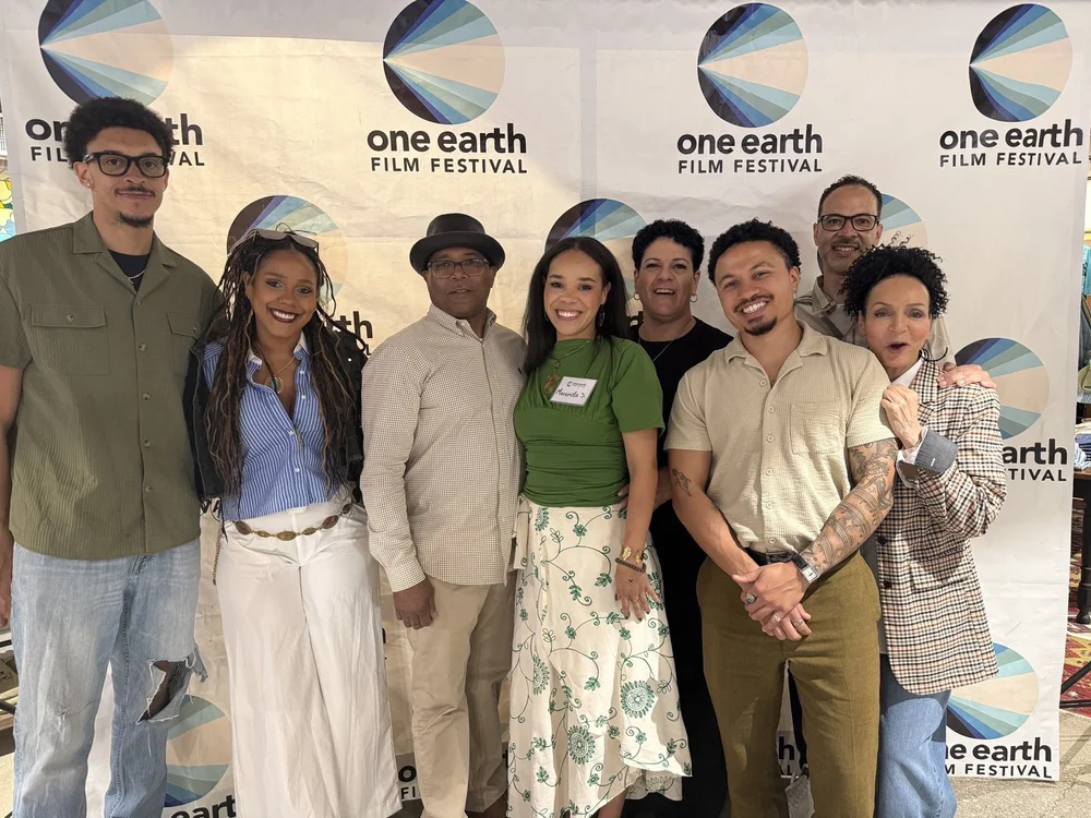 Seven people pose in front of a One Earth Film Festival backdrop at the 2026 “40 Acres” screening.