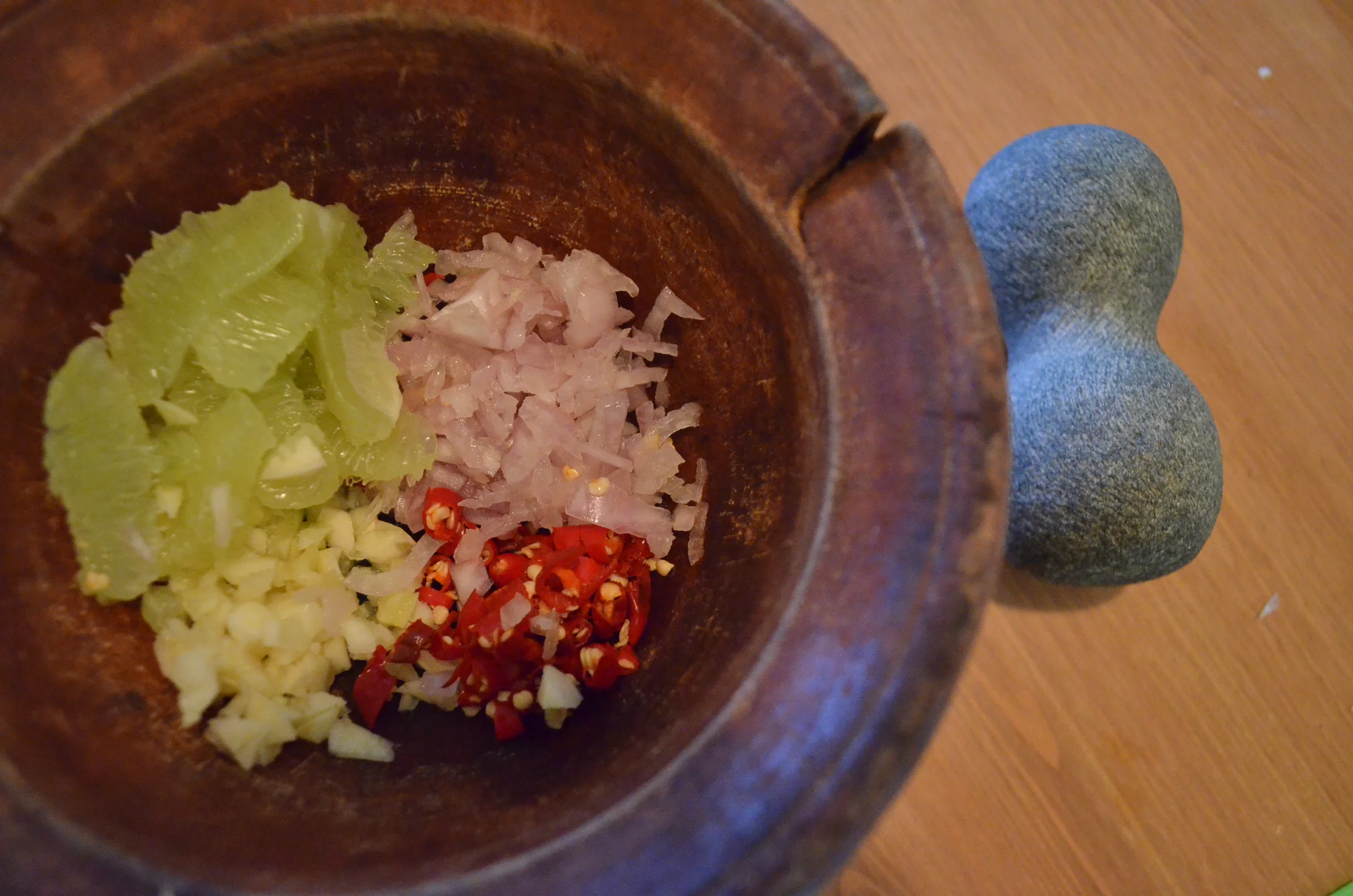 the lime segments, chiles, garlic, and shallots in a wooden mortar before mashing (Photo: Loa/Kathy Triệu)