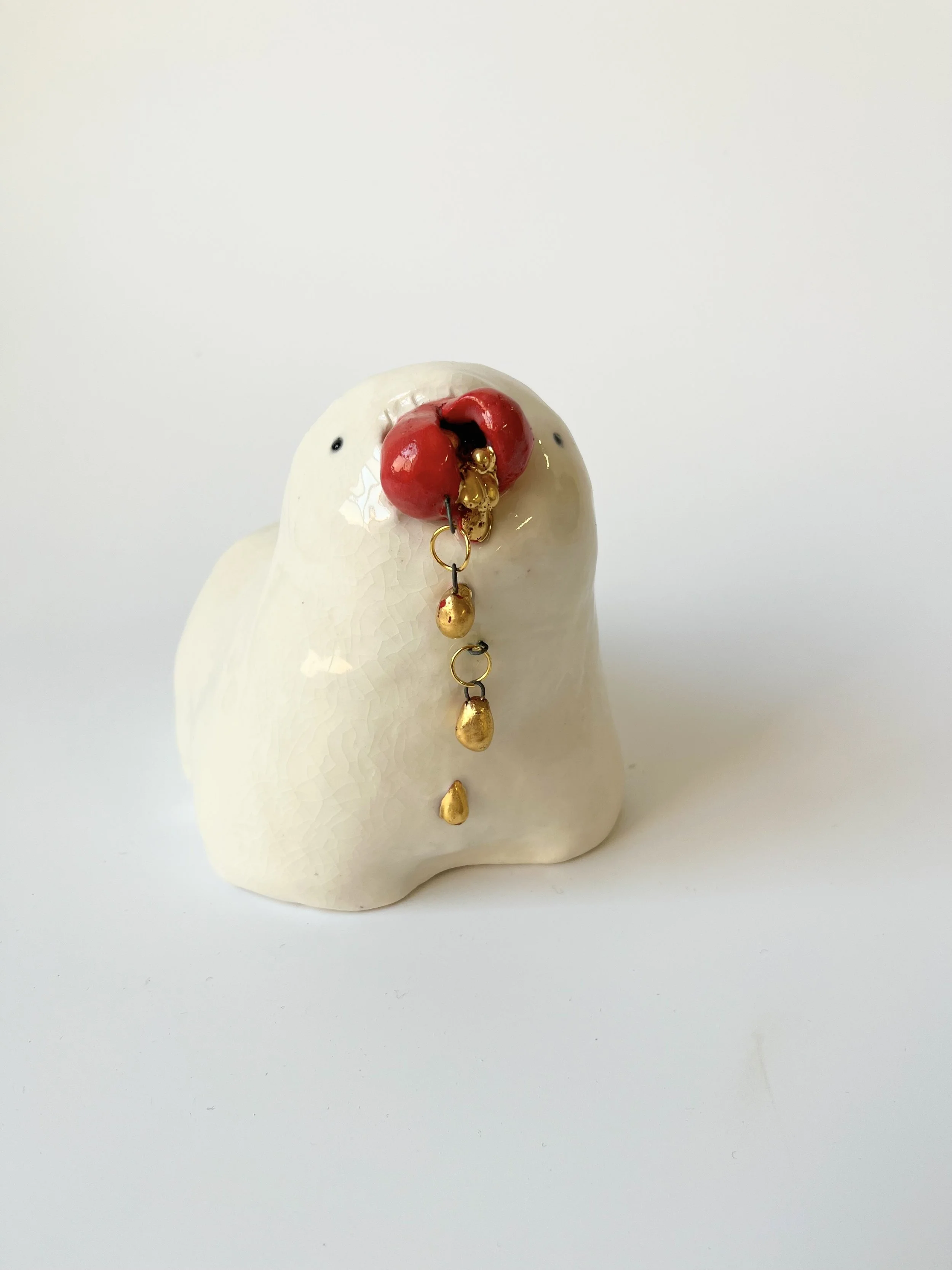 Porcelain teethie monster, holding a broken heart with drips of gold spilling out