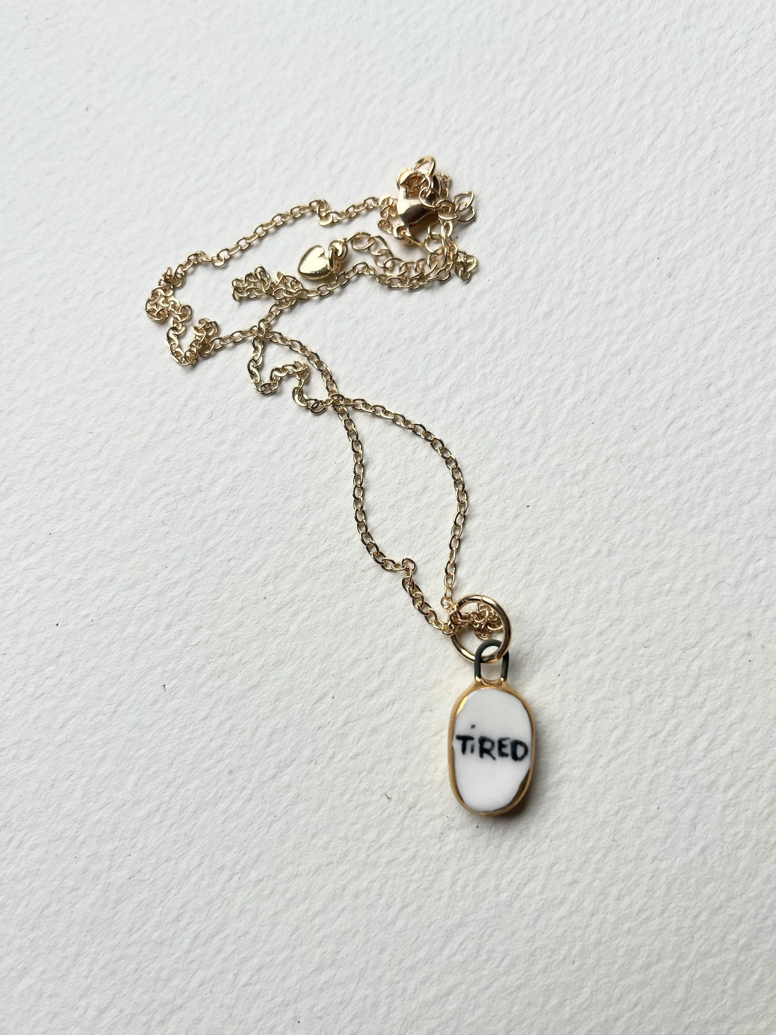 Tiny porcelain pendants with real gold rim and the word "tired"