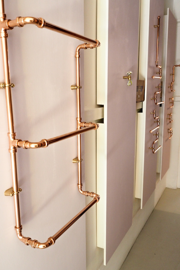 panels of pink from little greene paint co line the corridor of the forster inc hallway, showcasing dog's body copper pipework in various utilitarian purposes.