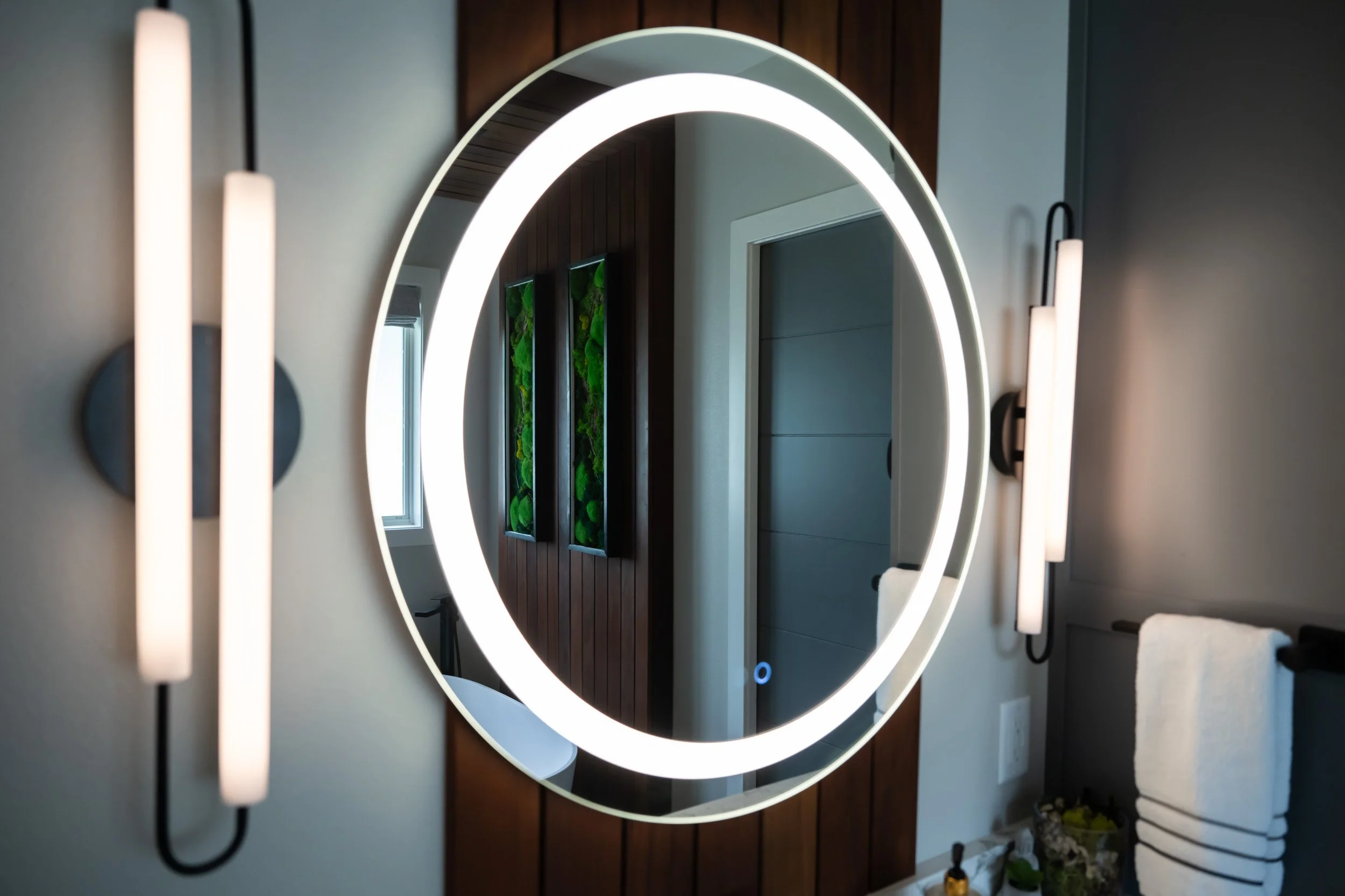 Focused view of the vanity mirror and light fixtures, capturing the teak accent by the bathtub