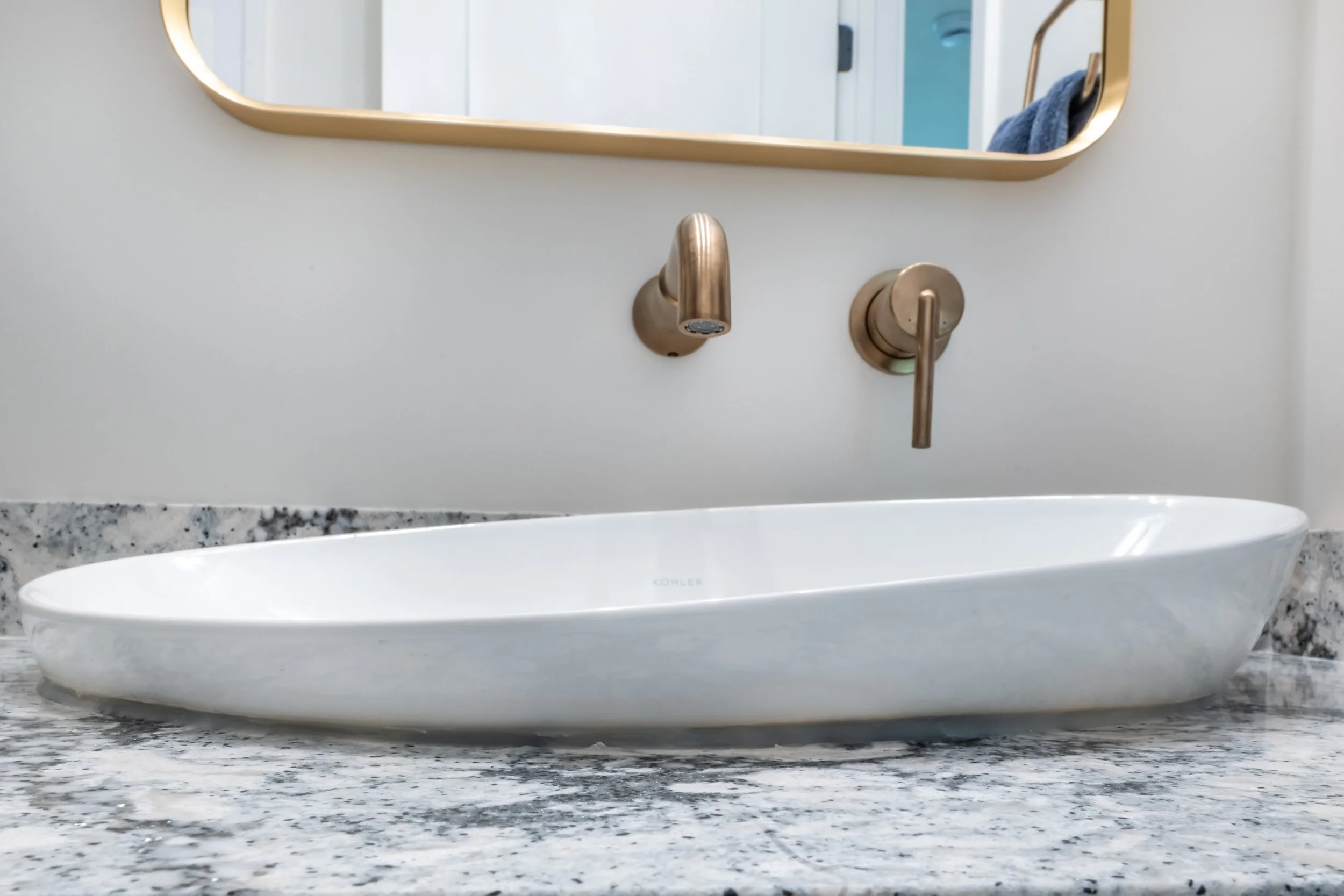 Close up view of the vanity sink, showcasing the Delta wall mounted faucet & Kohler mirror