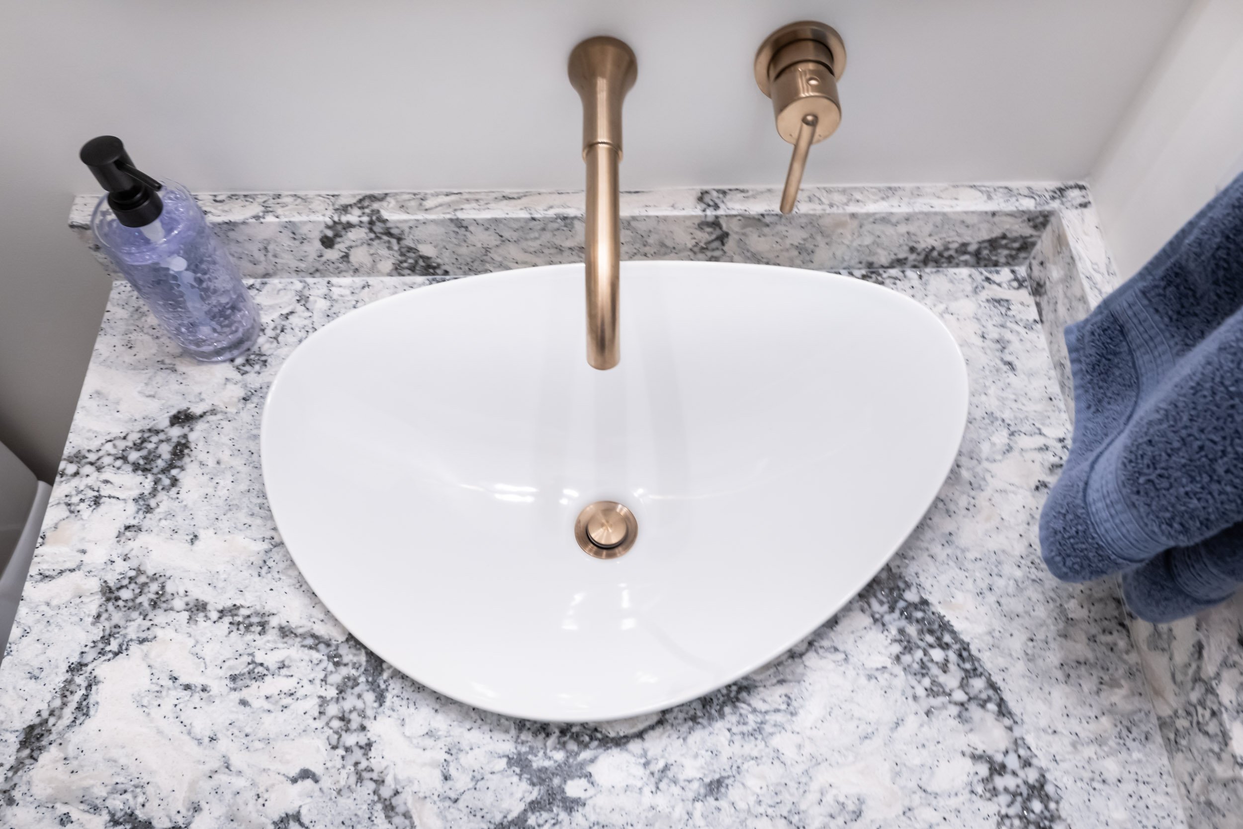 Close up view of the vanity countertop, showcasing the Cambria quartz, uniquely shaped Kohler vessel sink & the Delta wall mounted faucet