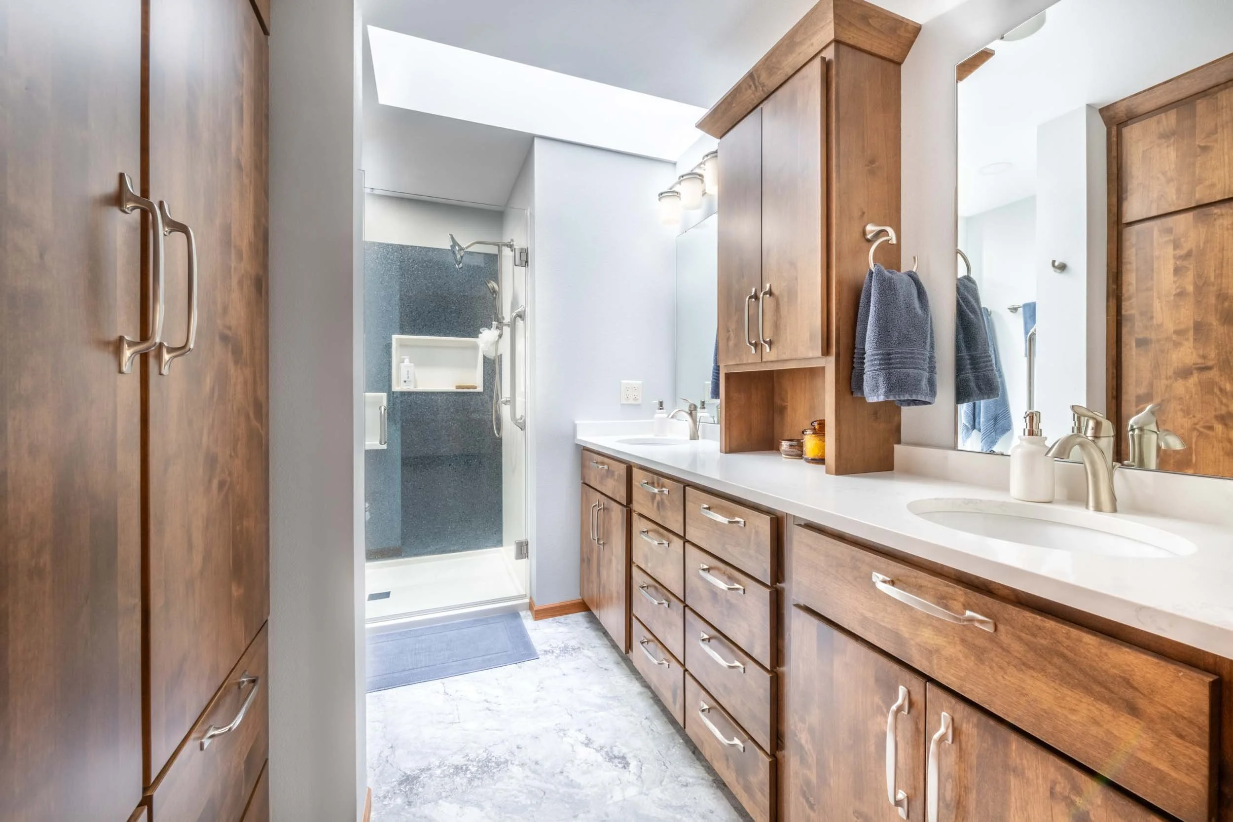 A bathroom with medium alder cabinetry, a black-and-white shower design, and a bright skylight