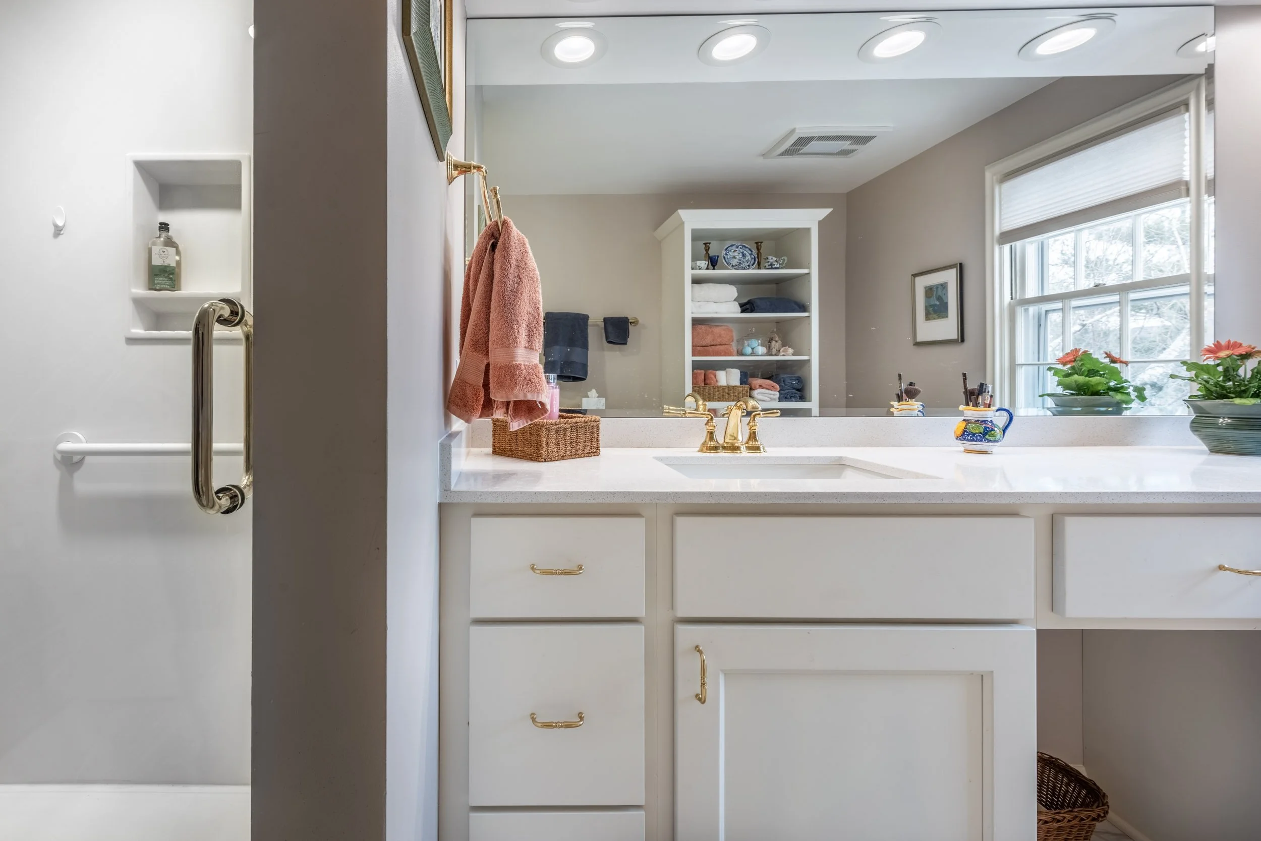 A white vanity with lots of lighting along side a off-white greyish shower that is easy to access