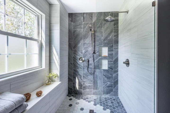 This bathroom remodel uses a mosaic of charcoal and grey-white tiles with a wet-room design