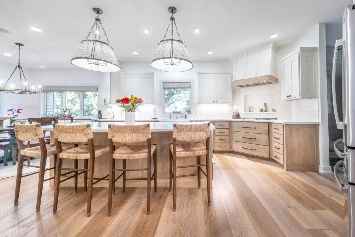 White upper cabinets and a stained wood floor with large island pendants