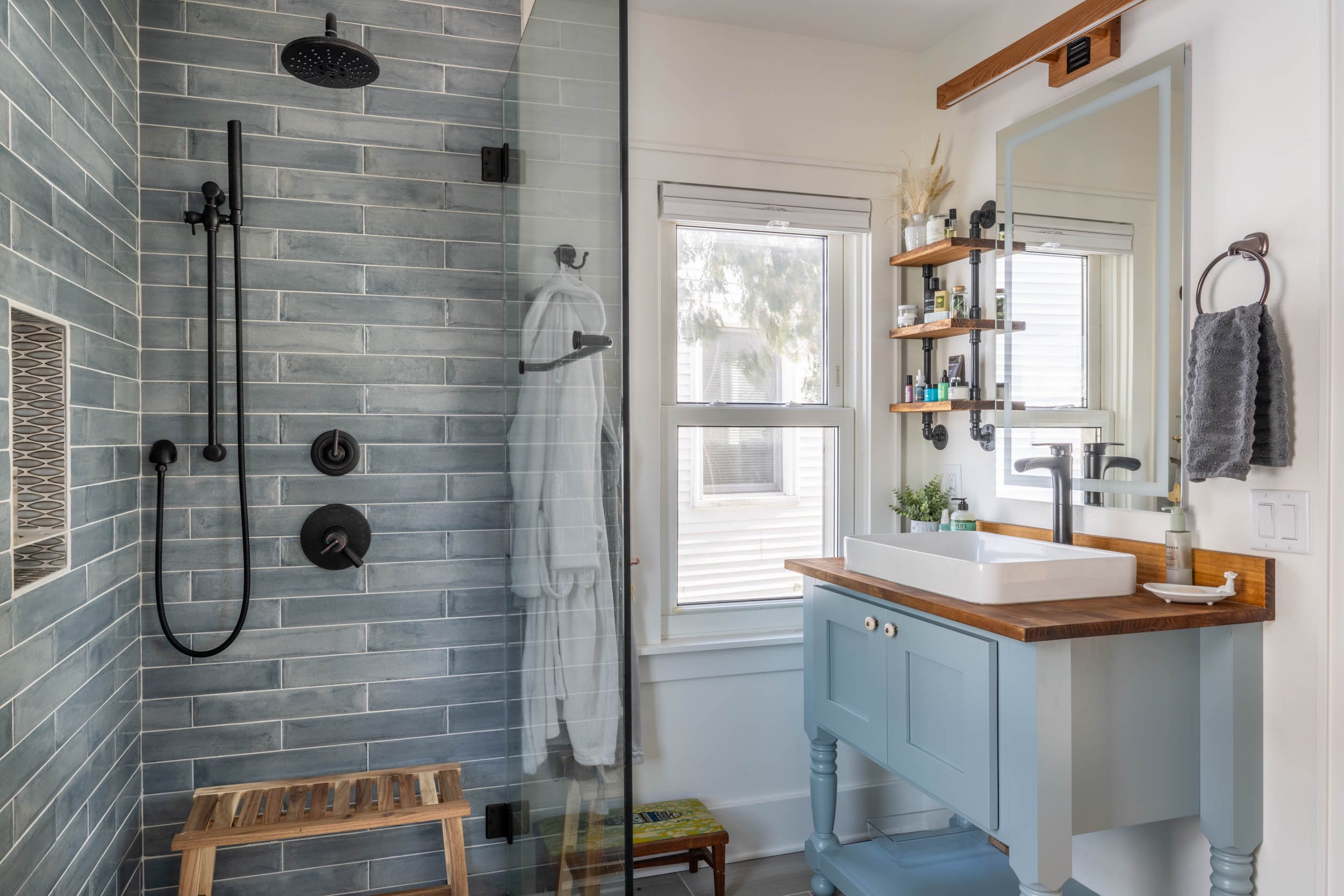 An image of the glass walled walk-in shower and vintage style vanity with window.