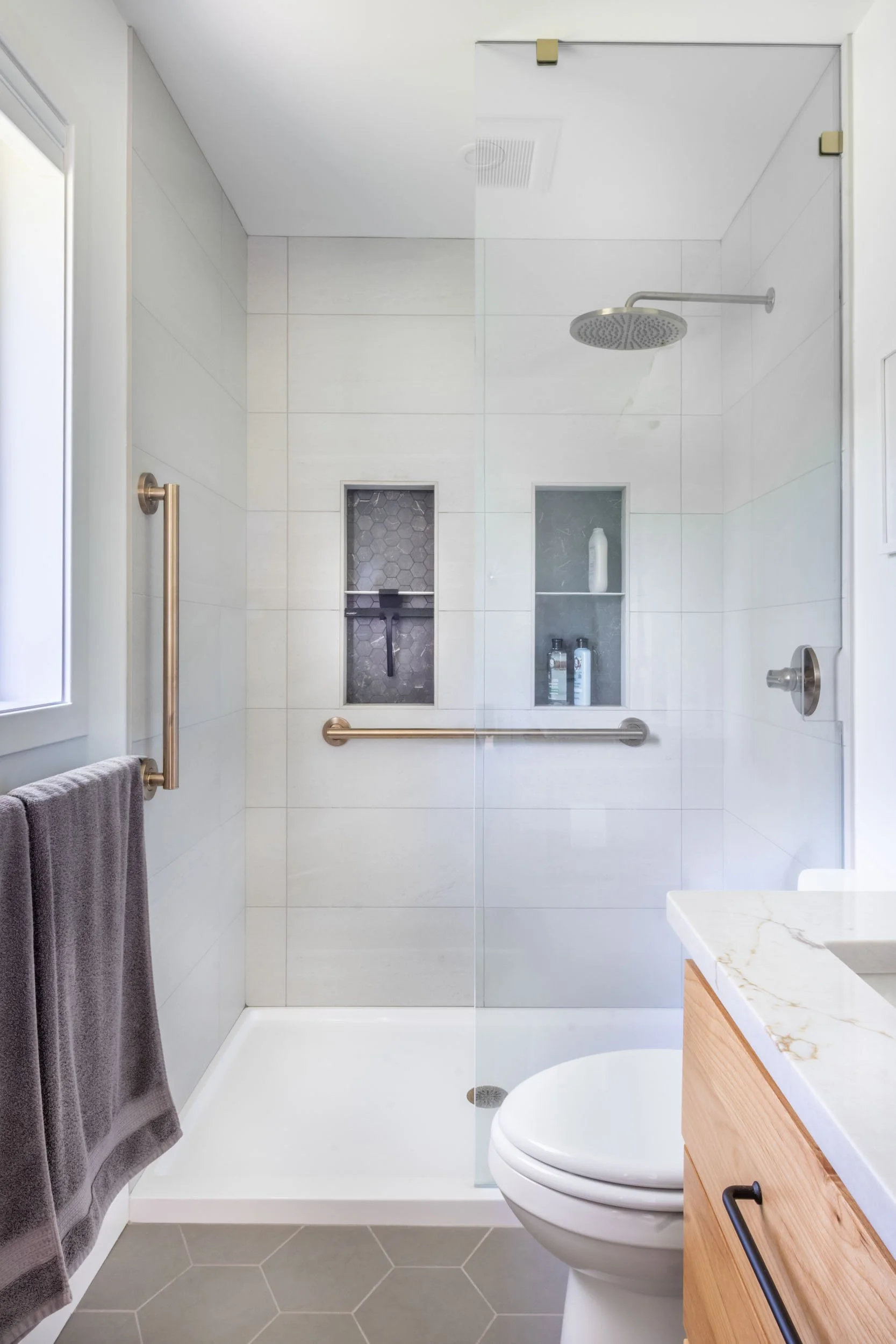 View looking at the primary bath tile shower, showcasing the Onyx shower pan, 21st Century Tile tile walls, the IntermateX mosaic tile niches and the champagne bronze Delta shower fixtures & grab bars