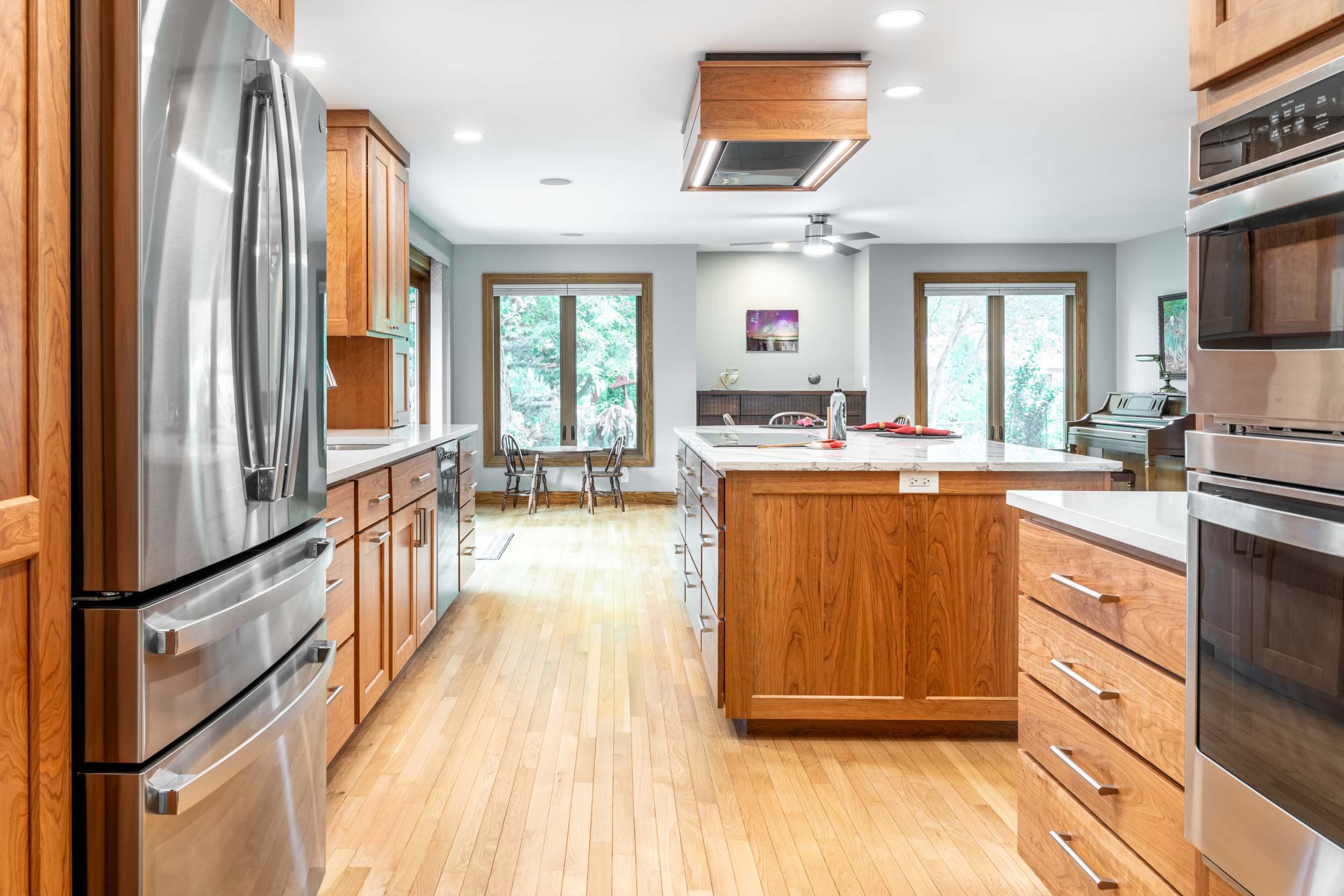 A cherry kitchen with maple floor, cooktop in island and cherry floating cloud hood over island