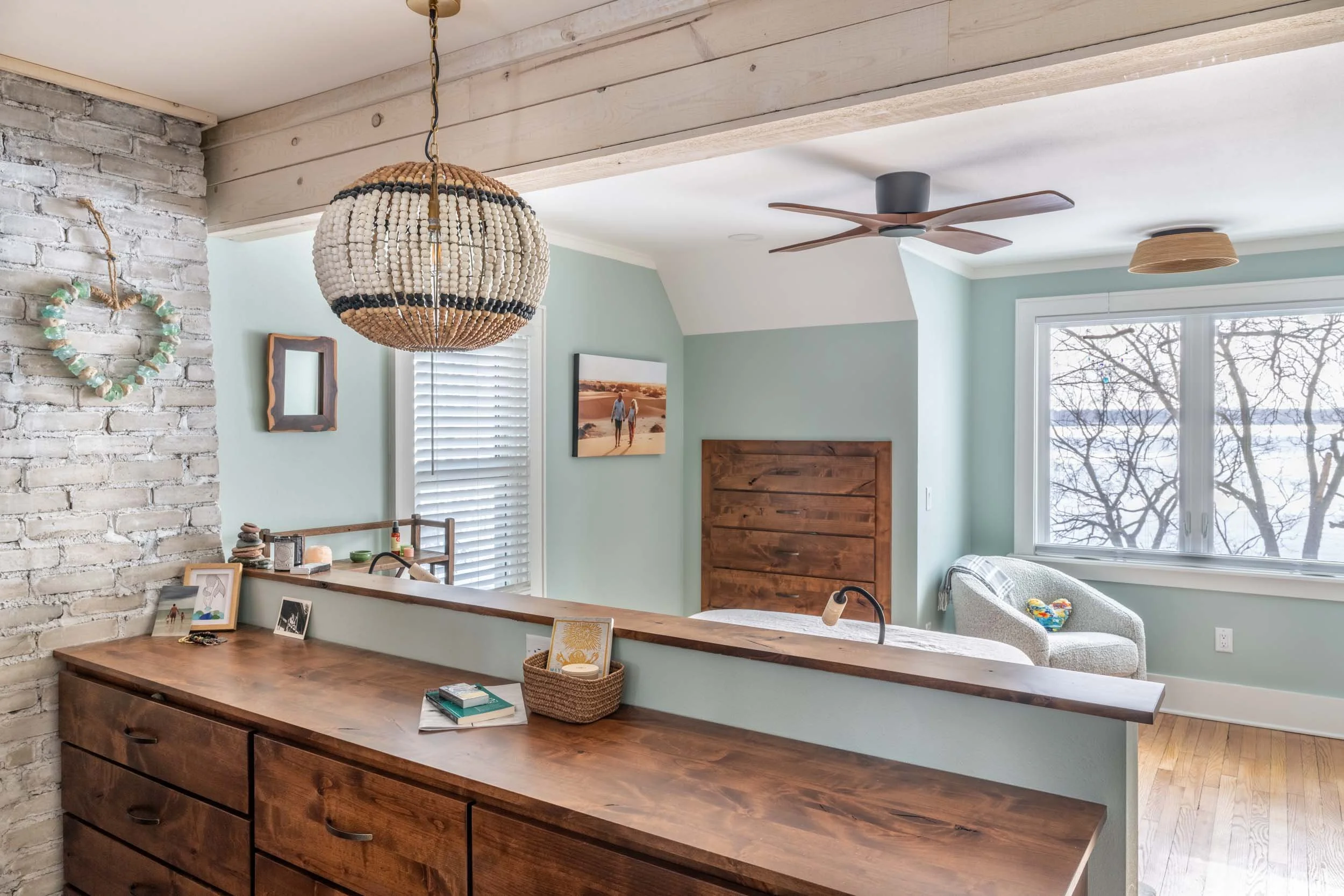 A view of the bedroom with built in dresser, seating area with windows and ceiling fixtures.