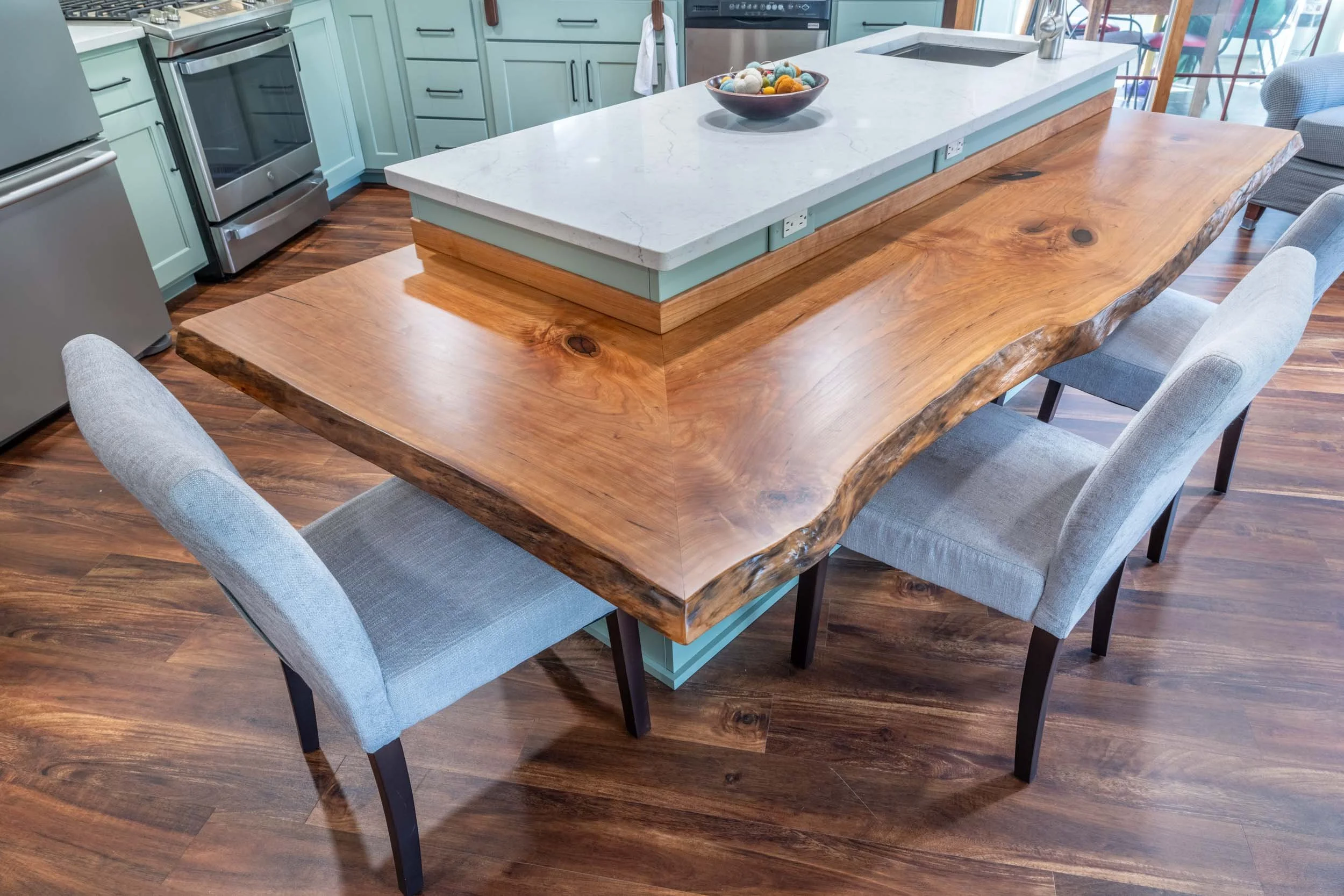 A painted island with light green cabinetry and a quartz top accented by a live edge wood countertop