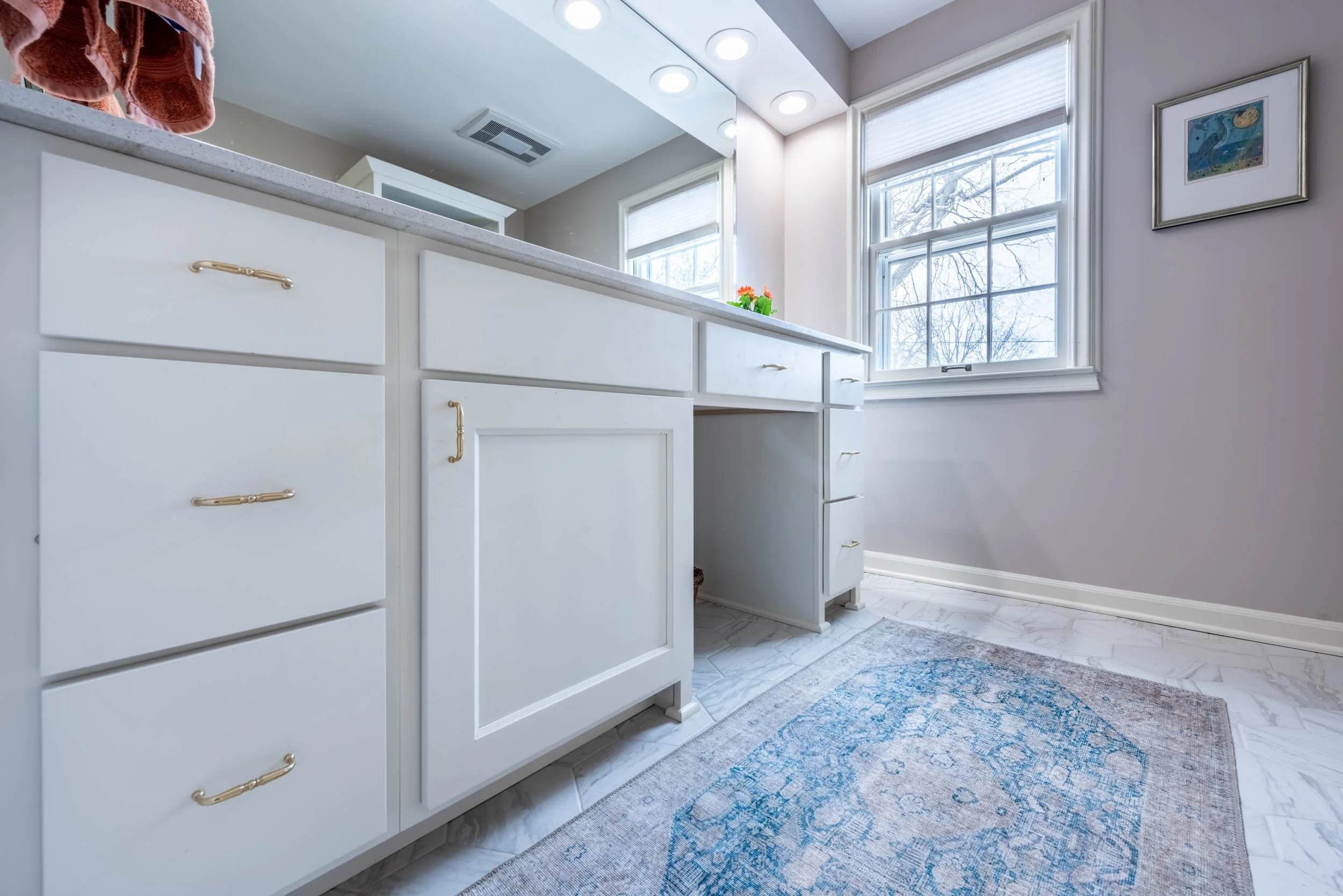 A white vanity in an older home with a large mirror and can lights in a soffit.