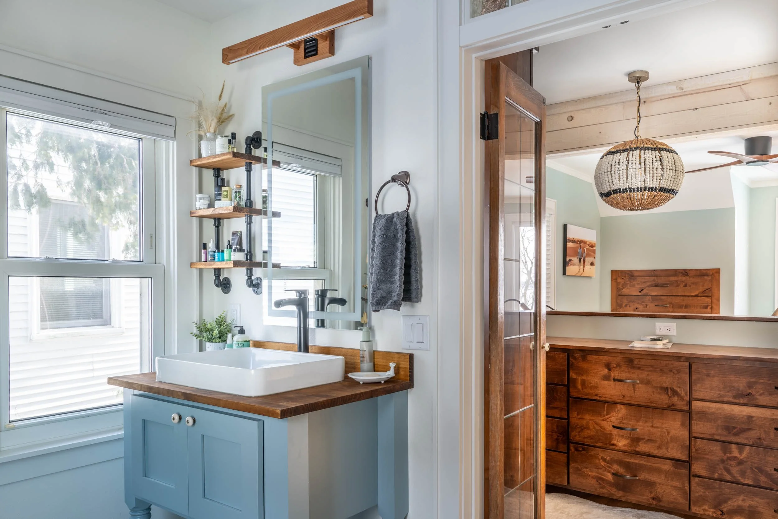 A bathroom suite with a vessel sink on a reclaimed wood countertop looking out to a dressing area with maple cabinetry