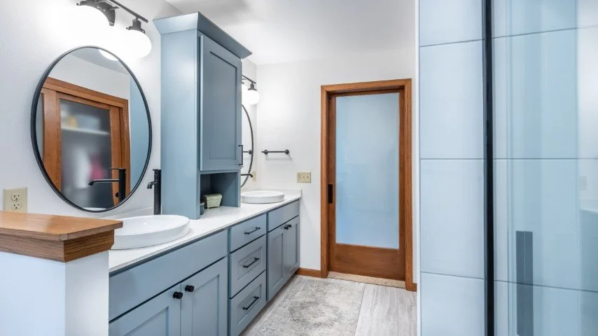 Frosted closet and bathroom doors, round mirrors, blue cabinetry, tile shower, and grey floor