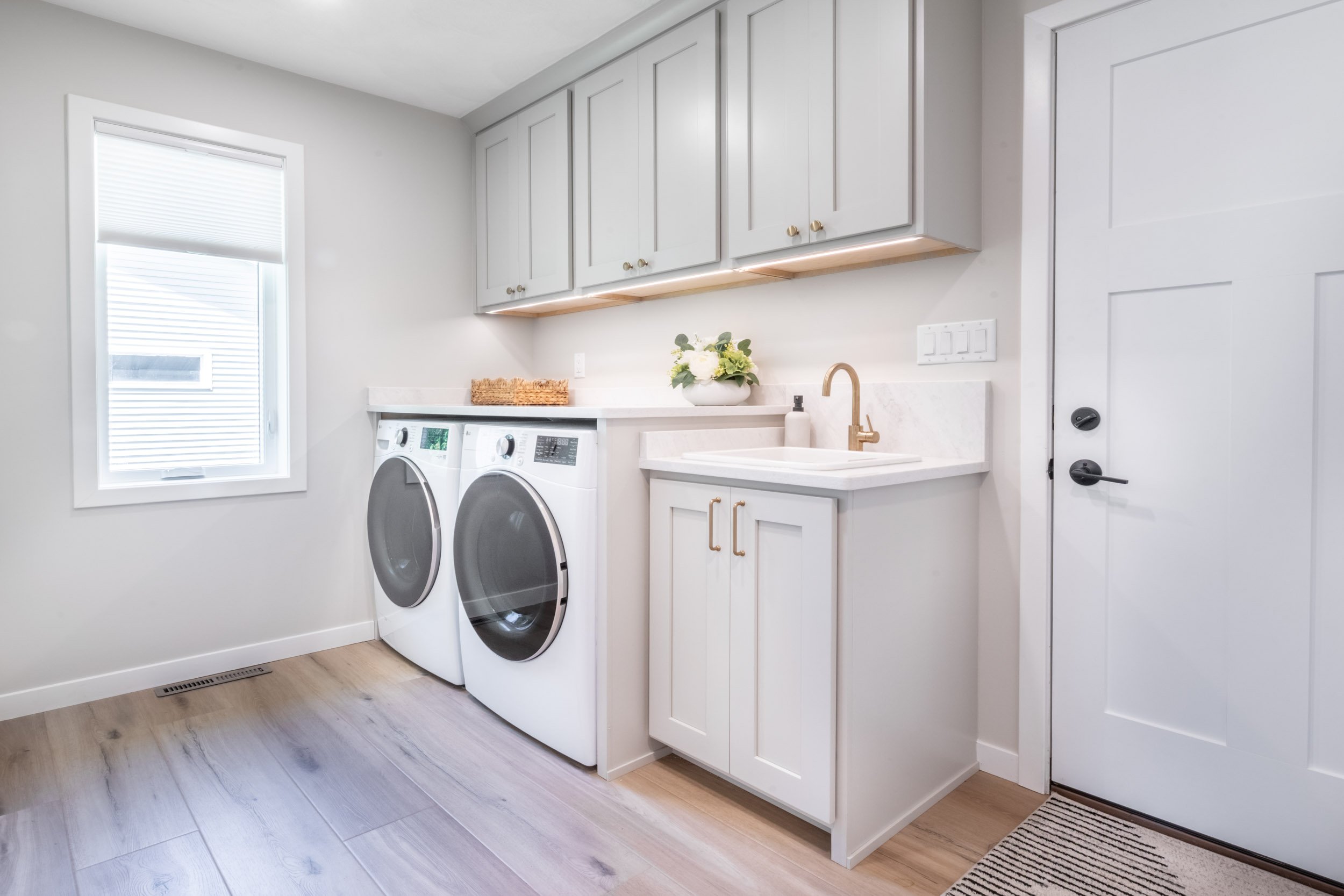 View from the kitchen into the laundry room, focusing on the cabinetry & built-in washer & dryer, with the Signature Hardware sink & Delta bar faucet.