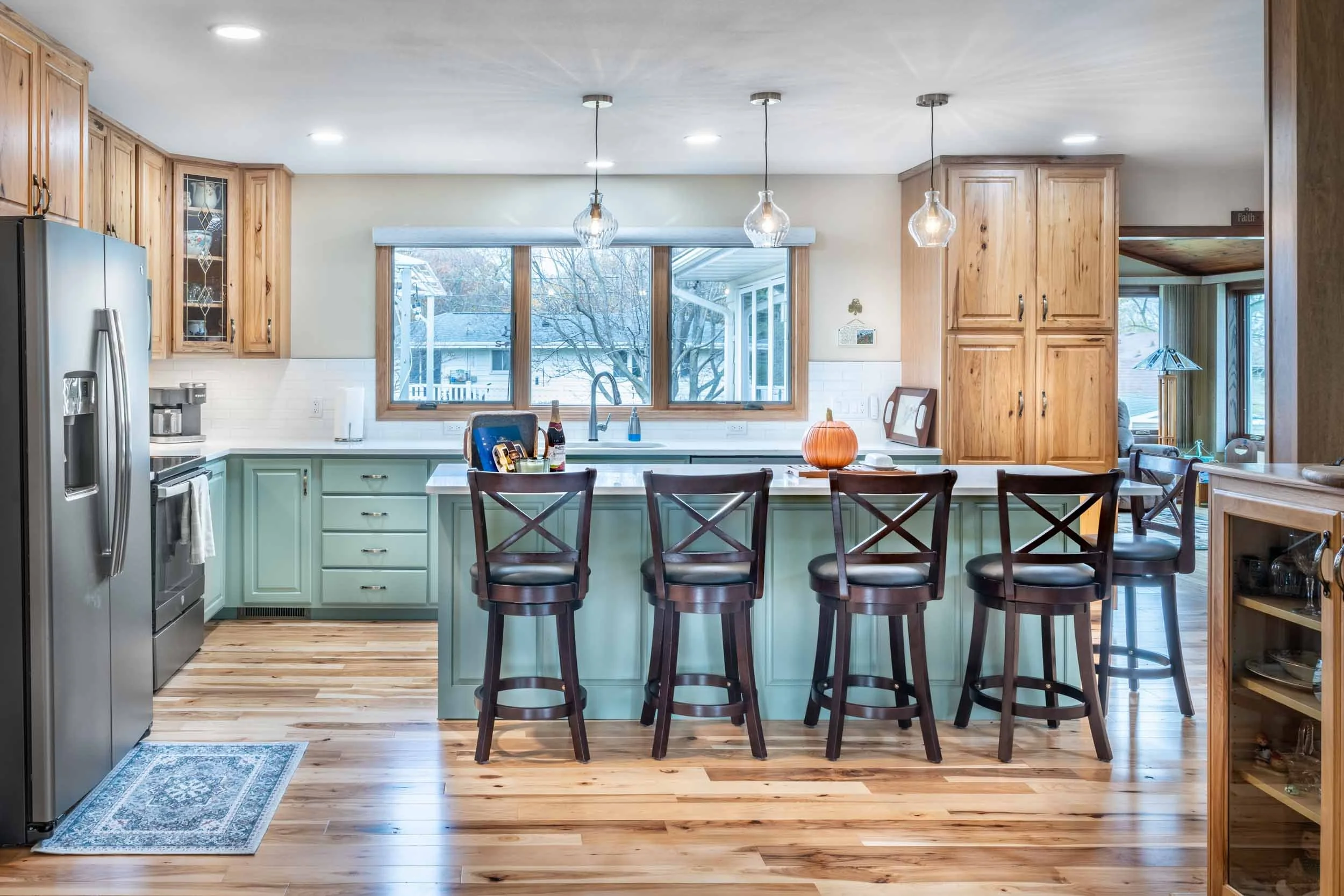 A bright kitchen with light green island and natural hickory cabinets