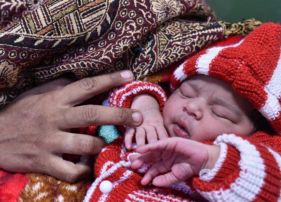 New Delhi, India, 12:20 am: Alka, 29, cradles her infant daughter, 2.7 kg (6 lbs.), at Lady Hardinge Medical College. She and father, Thakur Singh, will soon consult their priest to name the baby. India’s maternal mortality rate reduced from 280 deaths per 100,000 live births in 2005 to 174 deaths in 2015, due to such interventions as the Janani Shishu Suraksha Karyakran scheme which provides free maternity services for women and children.