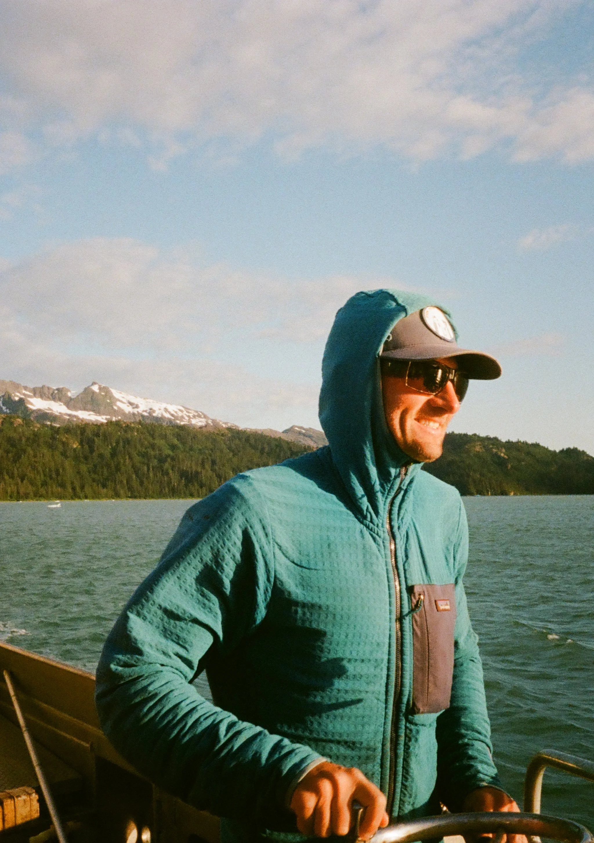 A man with a beard, wearing a blue knit beanie, a gray outdoor jacket, with a mountainous landscape in the background.
