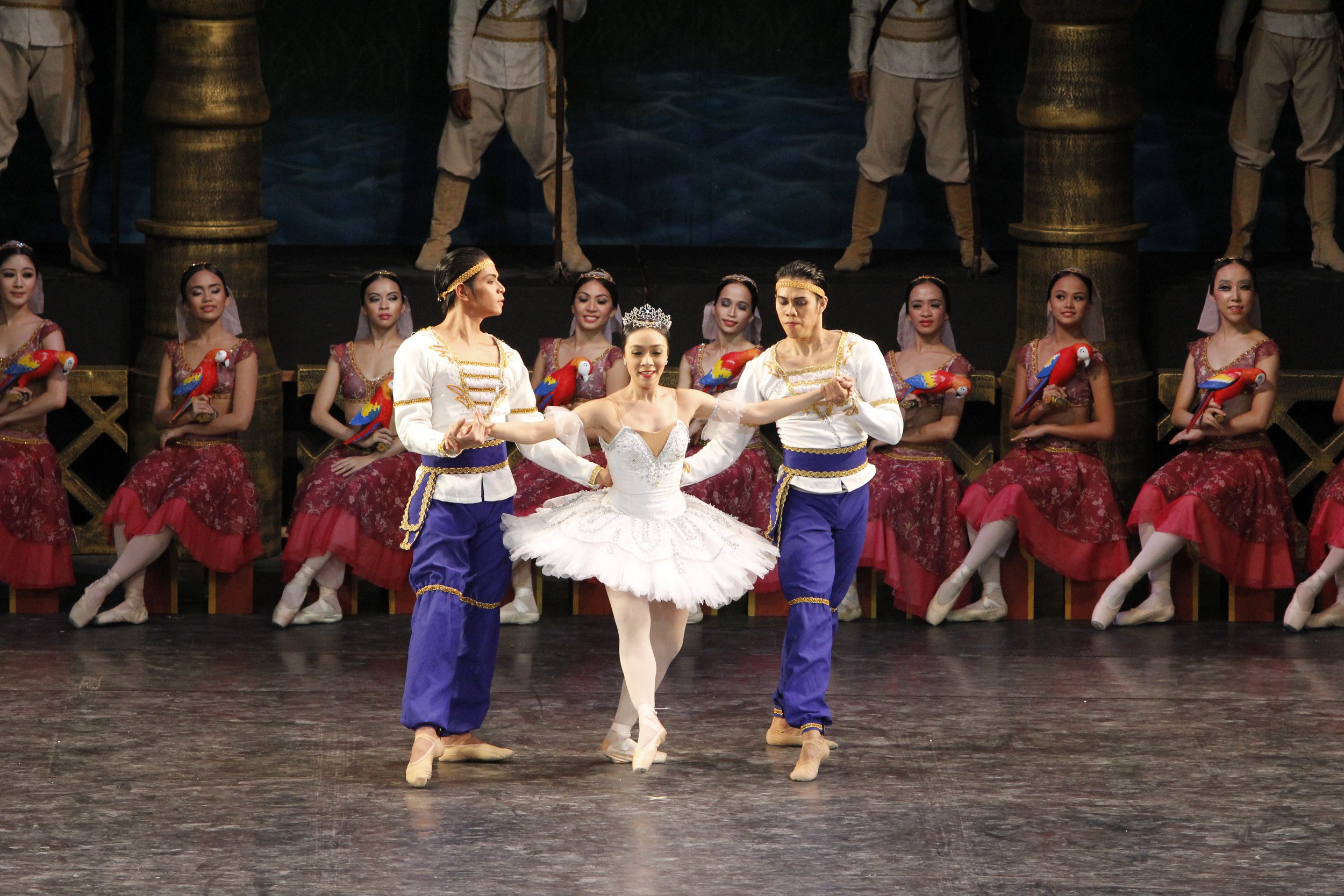    Purple-colored harem pants and sashes, worn by Mark Sumaylo (left) and Francis Cascaño, draw the eye in this scene from  La Bayadere  (2013) as they escort Gamzatti (Mylene Aggabao) in white, with the row of Parrot girls behind in red. Photo by Oc