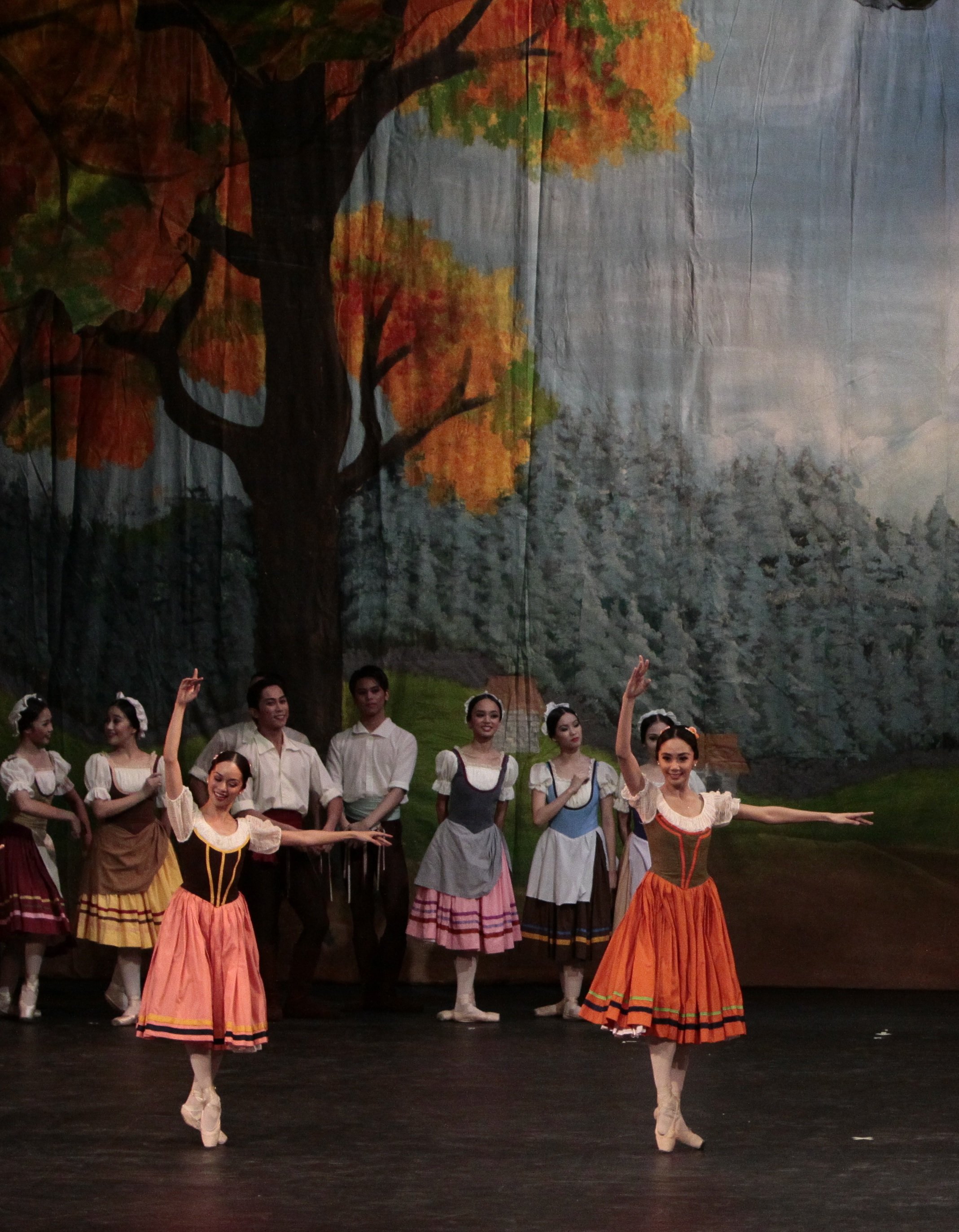    The peasant folk enjoy a village celebration in a scene from the ballet classic  Giselle  (2010). Two of Giselle’s gal pals (portrayed by Jennifer Olayvar and Zaira Cosico) coincidentally wear dresses in shades of orange, both pleasantly complemen