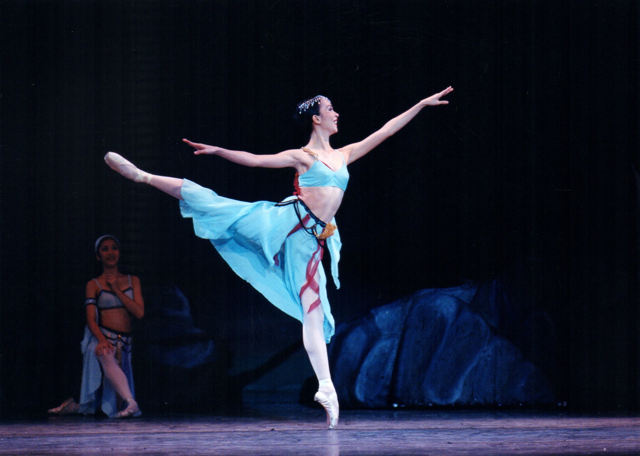    As Medora, Aileen Galinera channels the color of the ocean in her aquamarine wear in this scene from  Le Corsaire  (2002). Nimble on her feet, Medora is in a cheerful mood, unaware that danger lurks as a slave trader is about to abduct her and her