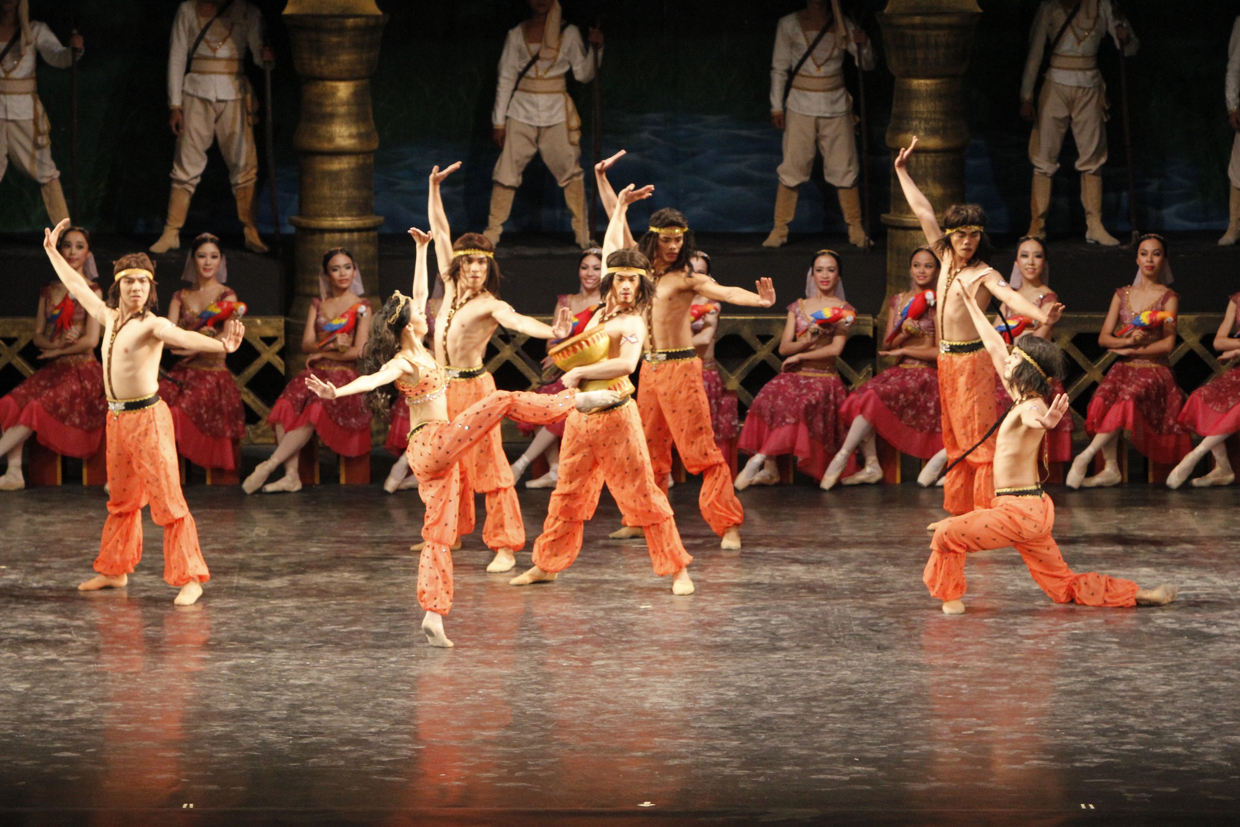    At Gamzatti and Solor’s betrothal in  La Bayadere  (2013), many ceremonial numbers are presented to entertain guests. Here, the performers clad in orange costumes rouse the crowd with their drum-thumping Indian Dance. Photo by Ocs Alvarez   