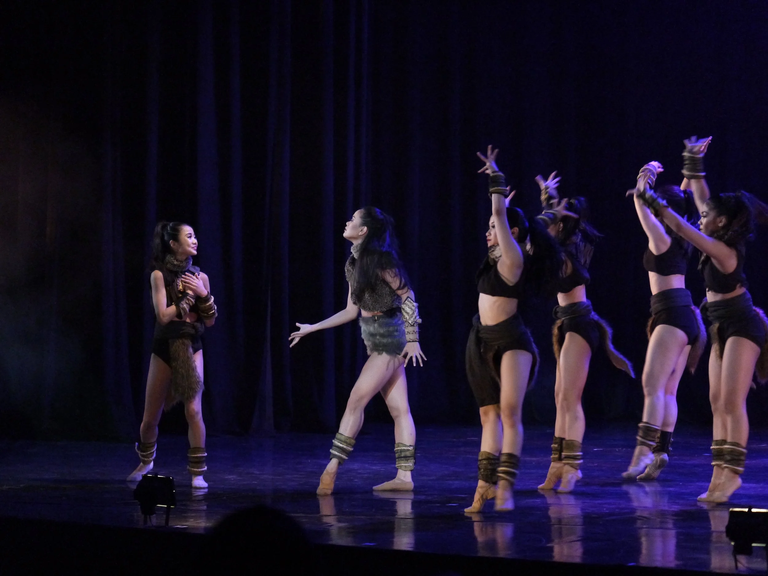    The queen of the Amazonas (Rissa May Camaclang, second from left) leads her group in welcoming back one of their own (Sayaka Ishibashi) as she recounts being accosted in the forest and then rescued by Prince Diego. The leader wears an ensemble of 