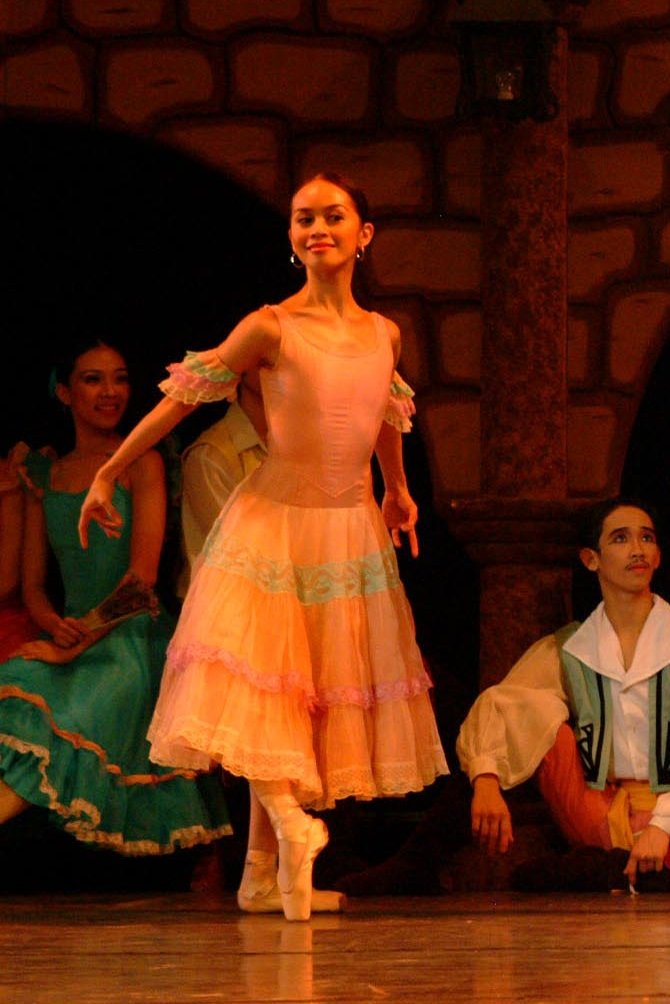    In  Don Quixote  (2004), one of Kitri’s friends (Jenny Olayvar) wears a tutu with a tiered peach skirt accented with multi-colored laces mirrored in the armbands. Joining everyone having fun at the town plaza, she turns and twirls, her skirt flari