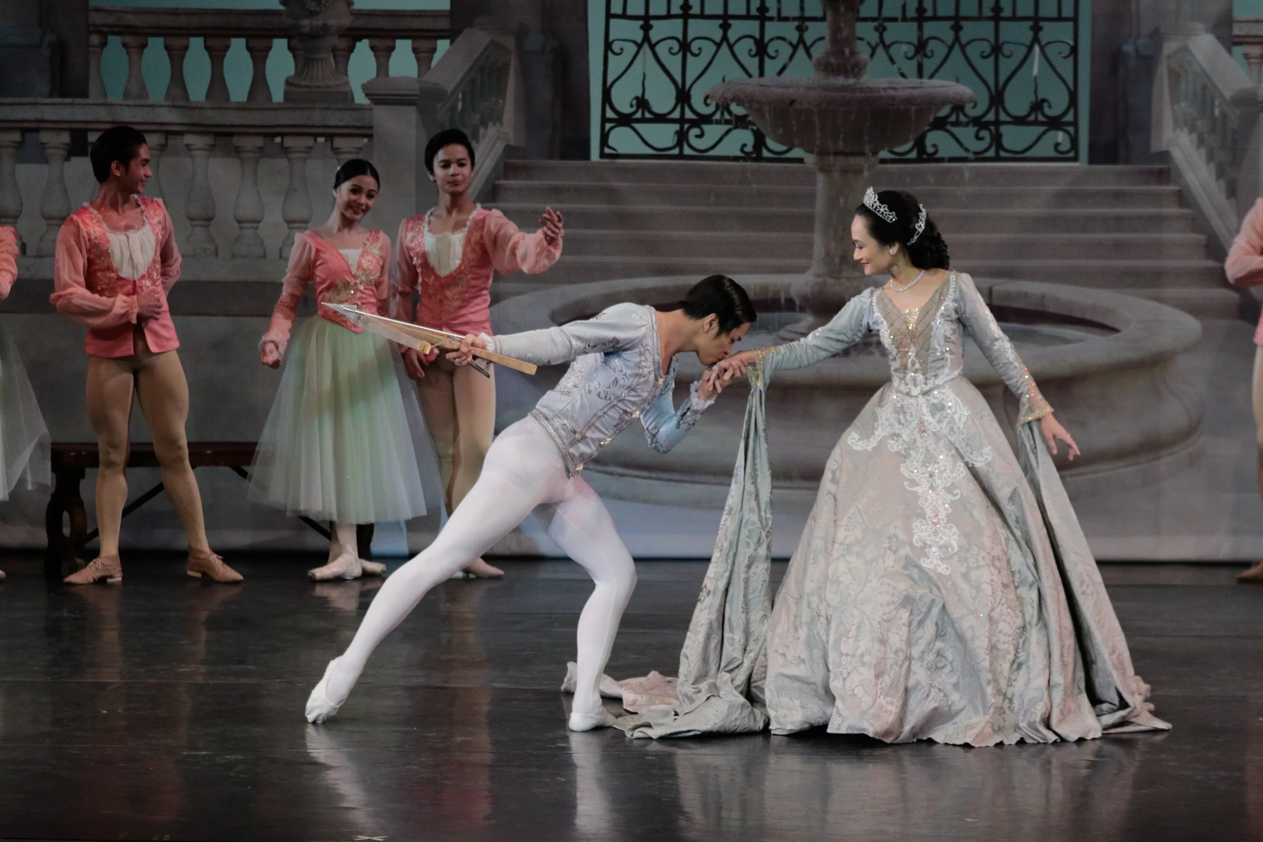    Resplendent in a silver gray gown, the Queen Mother (Lisa Macuja Elizalde) in  Swan Lake  (2017) has just given Prince Siegfried (Mark Sumaylo) a bow for his twenty-first birthday. Wearing finery in a similar color, the prince kisses his mother’s 