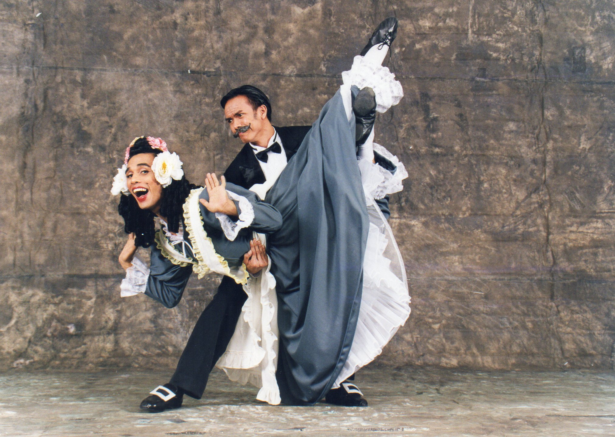    Wearing a voluminous gray dress with white frills and ruffles all over, Mother Simone (Christopher Mohnani) enjoys a light moment with wealthy landowner Thomas (Marcus Tolentino). In the English countryside-set comic ballet,  La Fille Mal Gardee  
